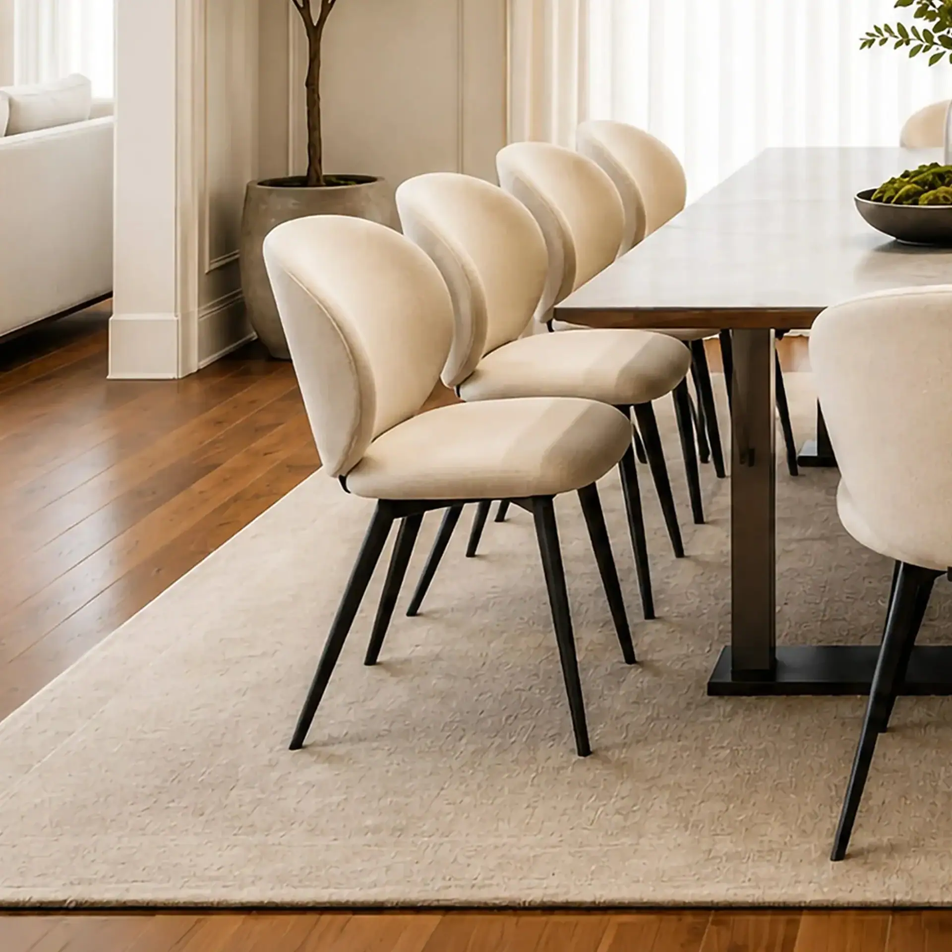 Elegant beige dining chairs with black legs around a wooden table in a bright room.