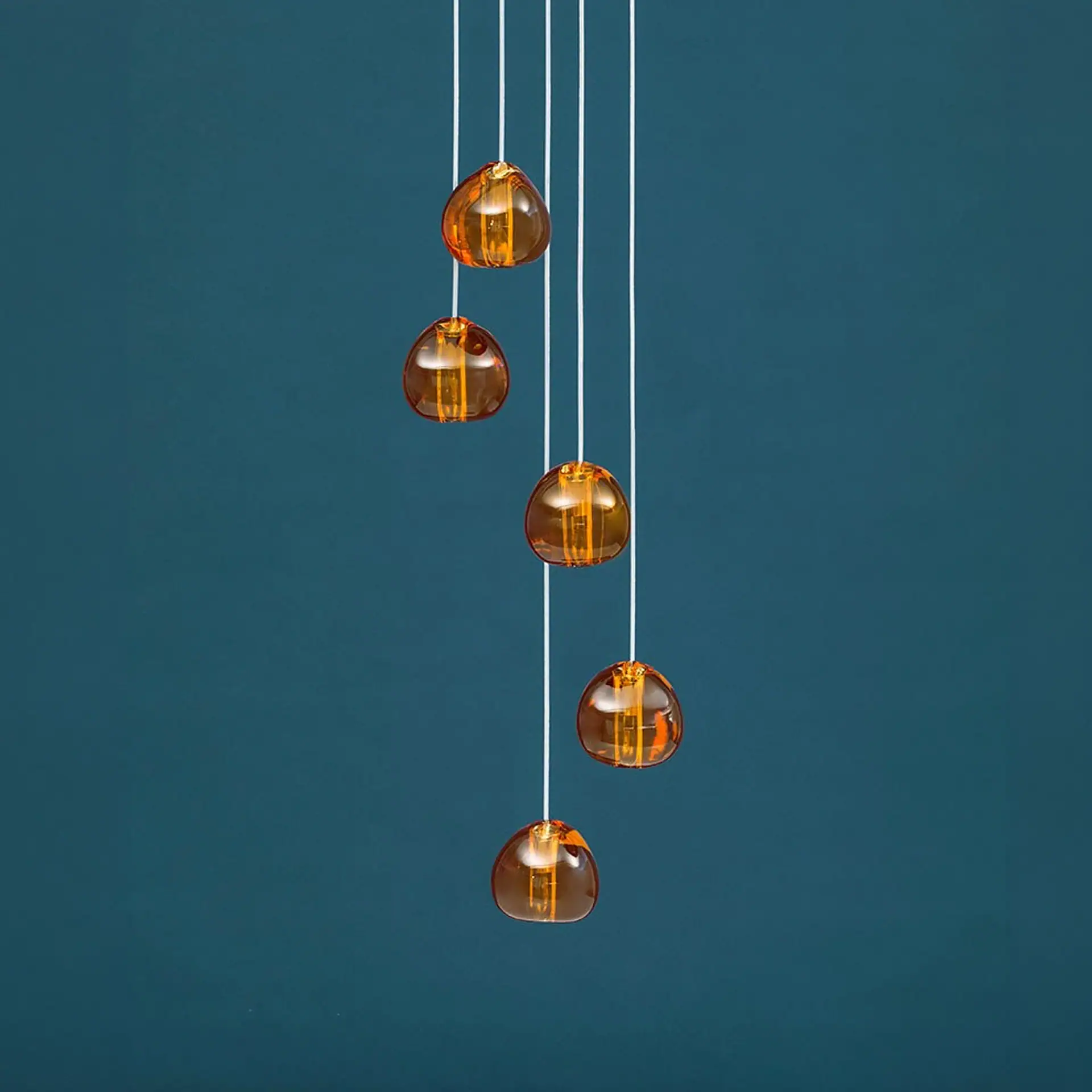 Five amber-colored, tear-drop shaped glass pendant lights hanging at different heights against a dark teal background.