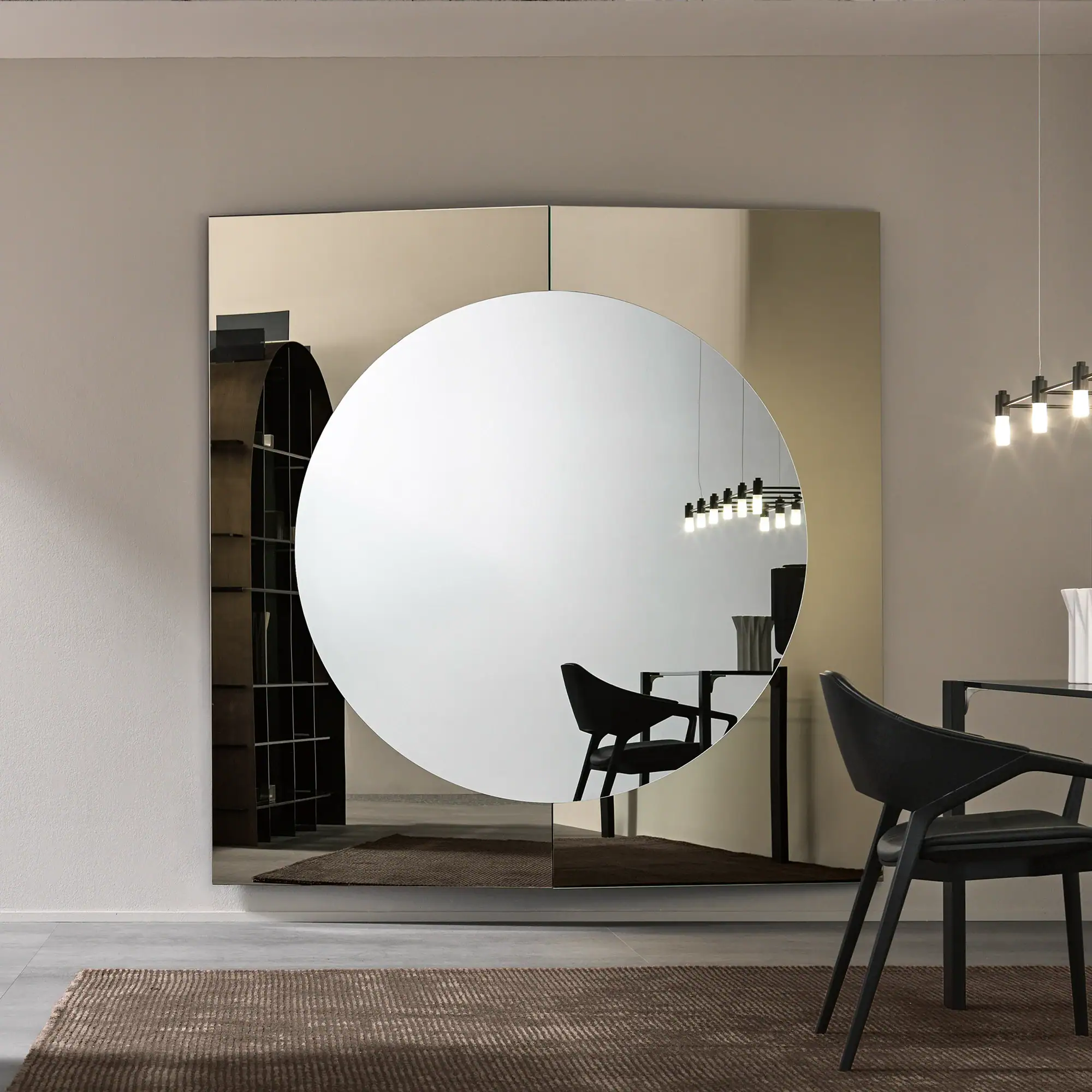 A large, multi-panel mirror with a central circular mirror reflecting a modern dining room with a black table, chair, and linear chandelier, set against a light taupe wall and a brown textured rug.