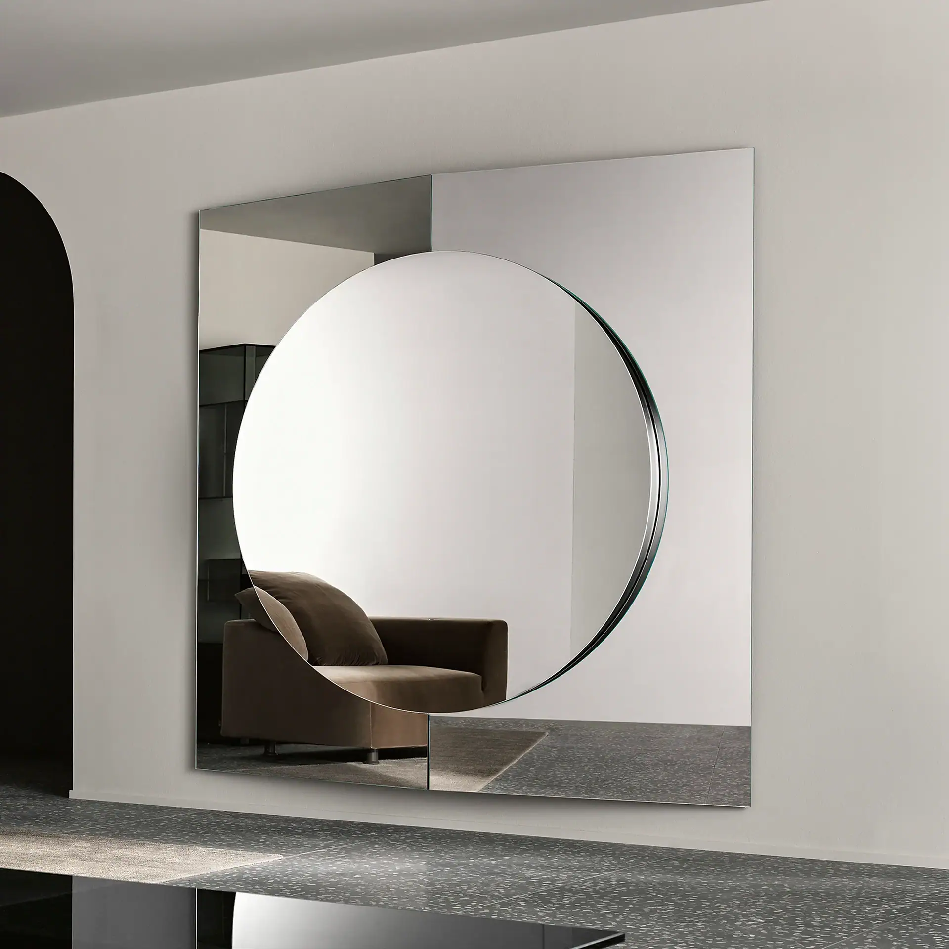 A large rectangular mirror with a circular mirror inset, reflecting a brown armchair in a modern room.
