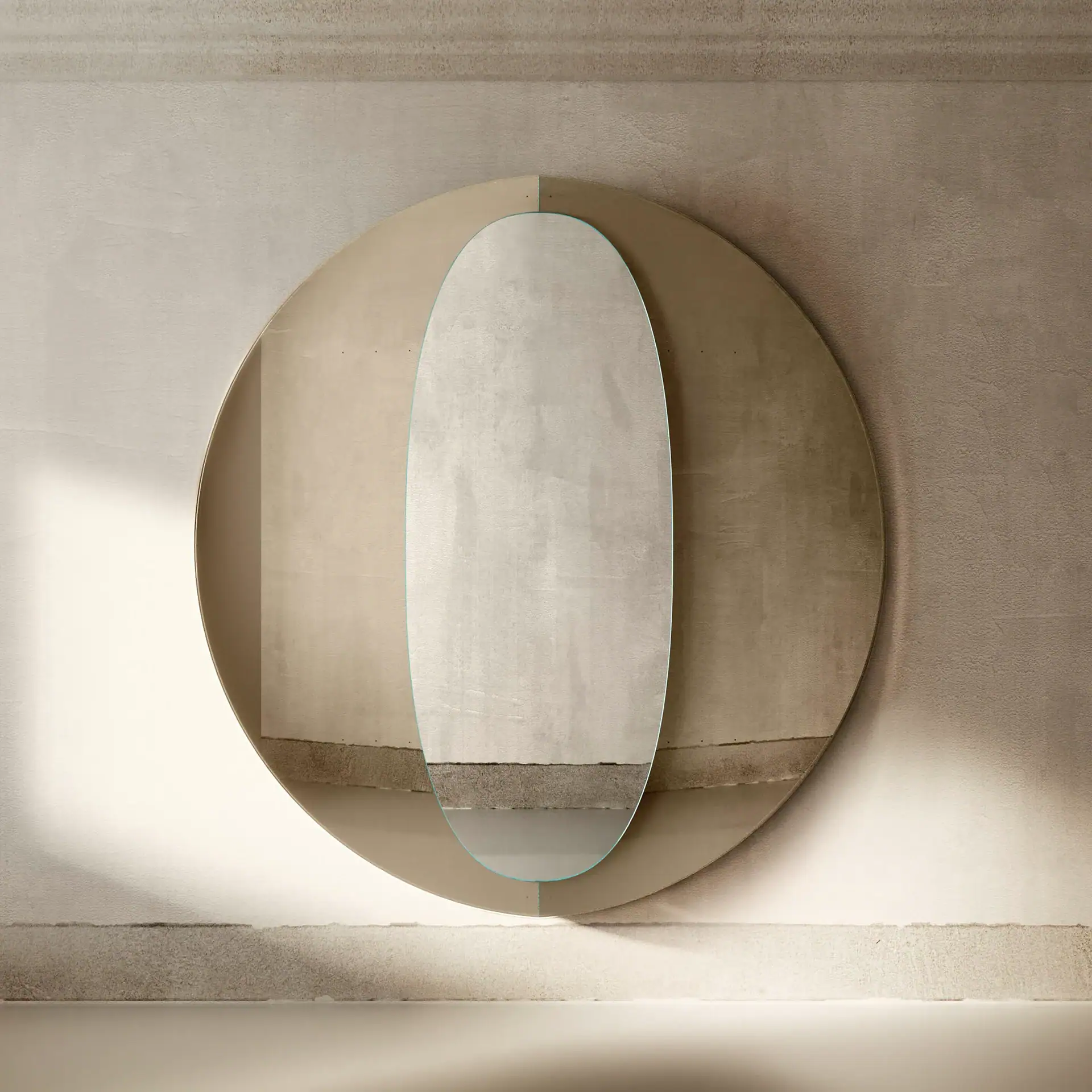 An oval mirror with a blue edge layered over a large, two-toned circular panel on a textured beige wall.