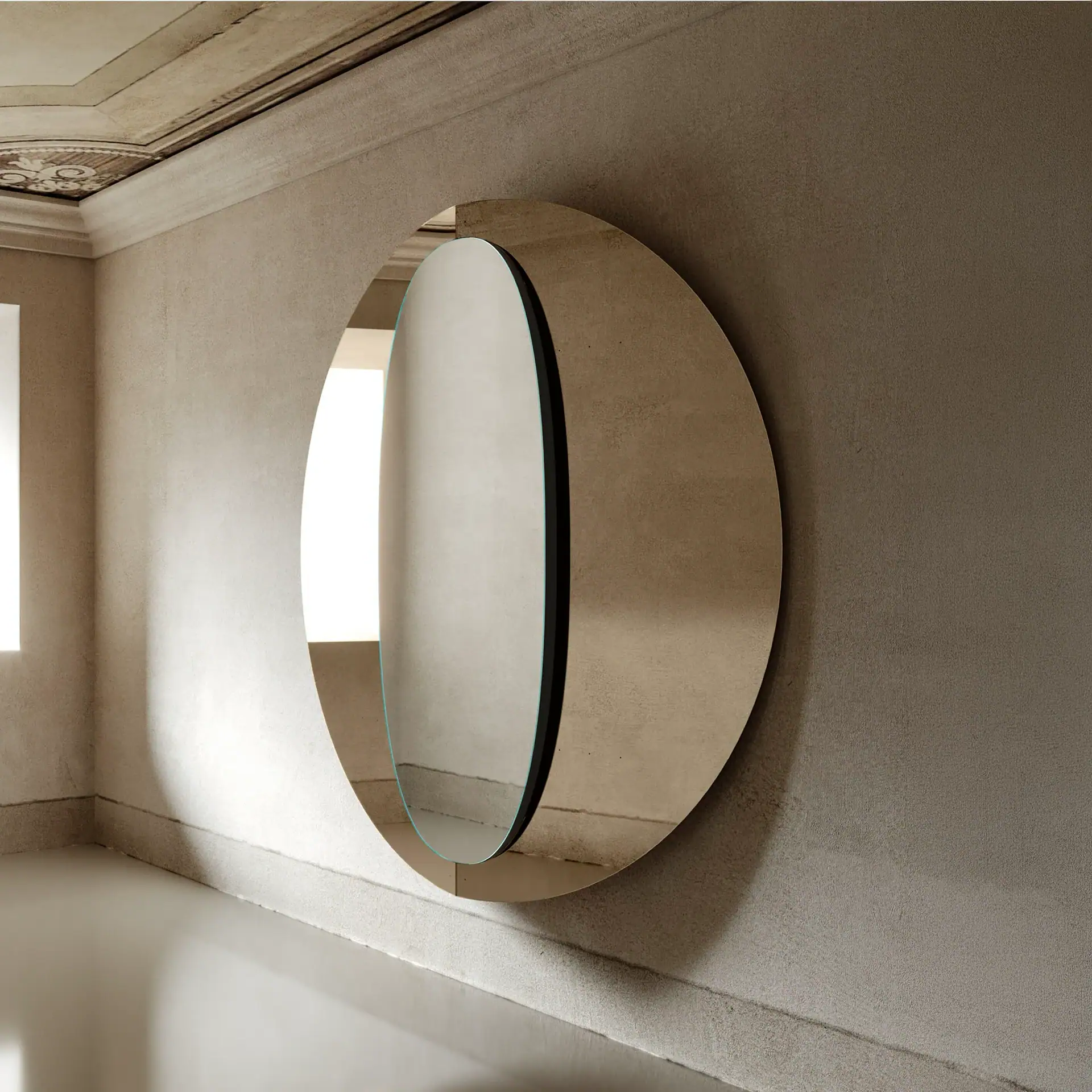 A large, round, modern mirror with a split design hangs on a textured beige wall, reflecting a bright window.