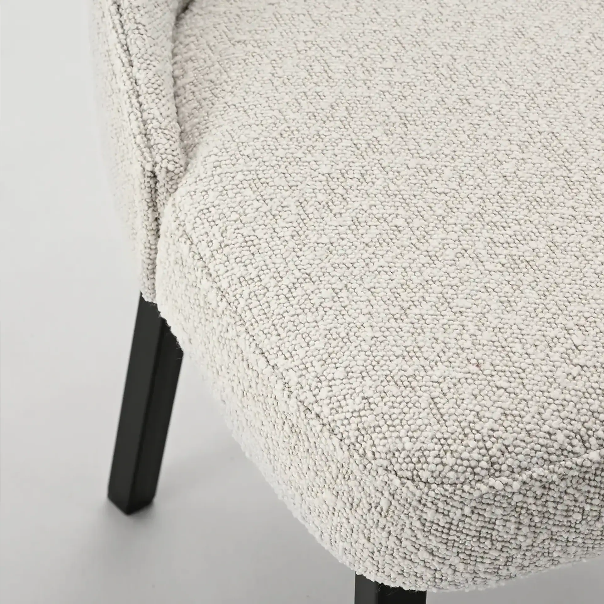 Close-up of a textured beige armchair with black wooden legs.