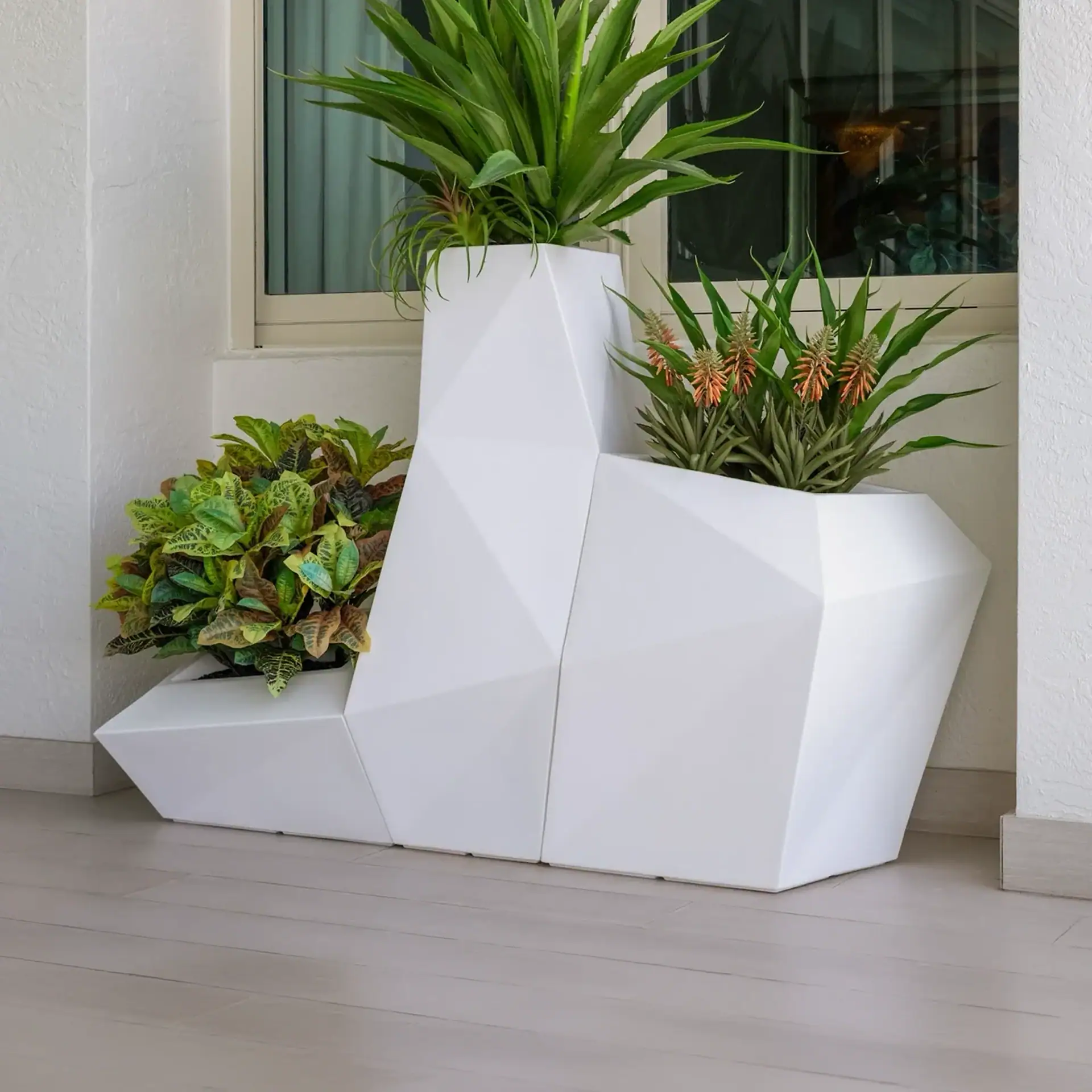 White geometric planter with lush green plants outside a window.