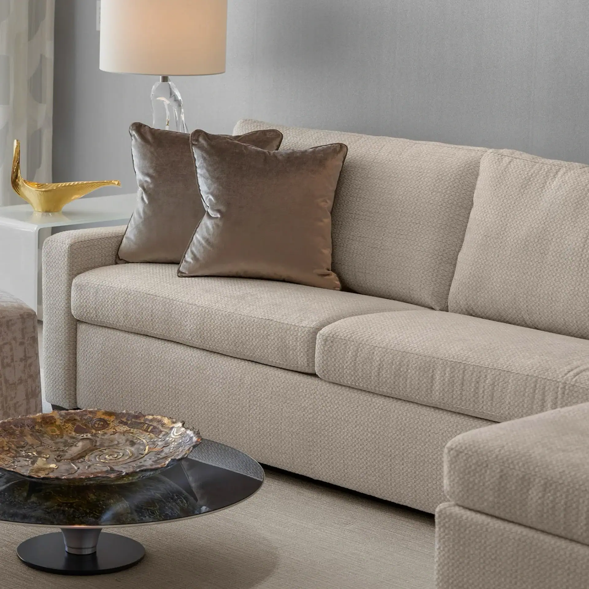 Sklar Furnishings beige fabric sofa with two brown pillows in a modern living room.