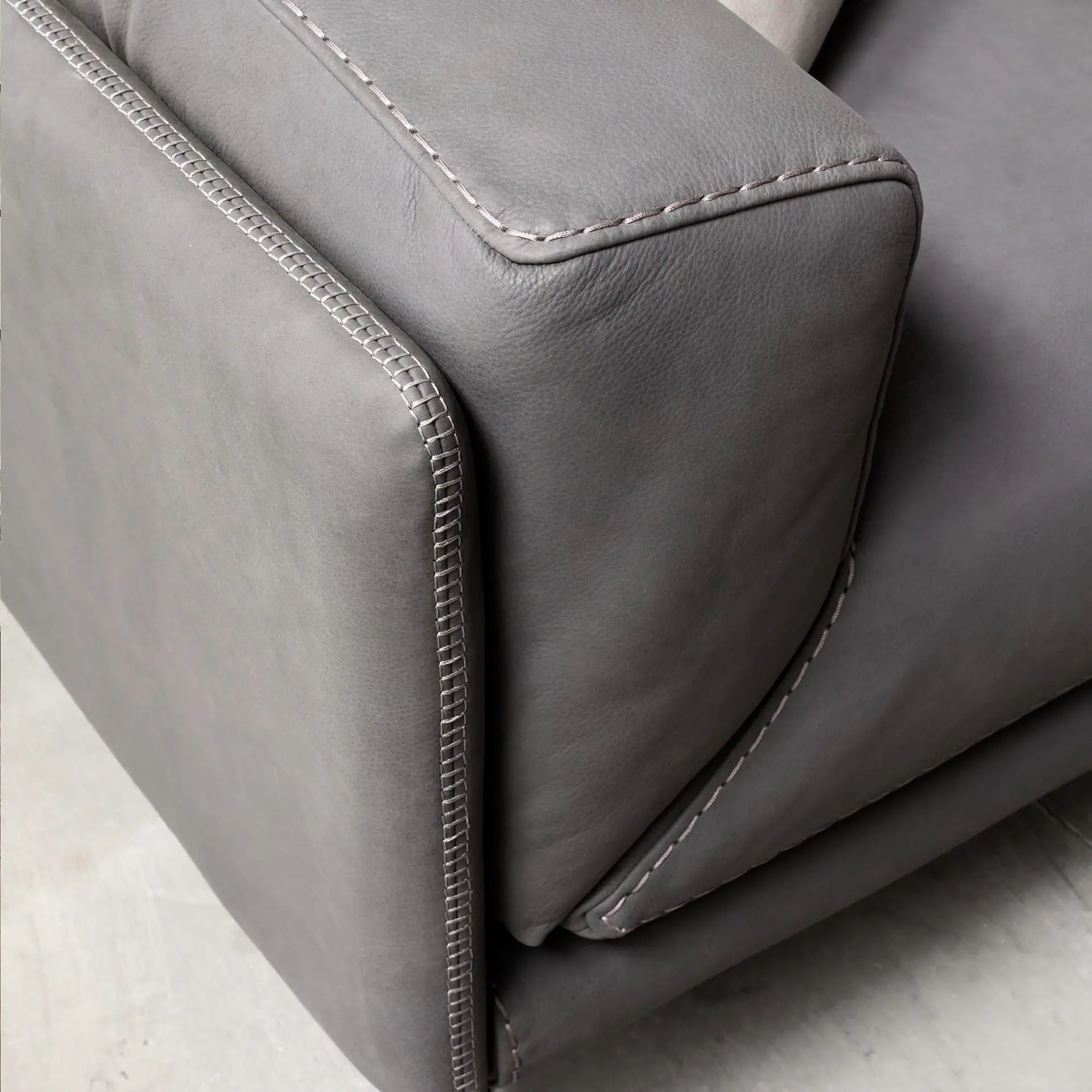 Close-up of a gray leather sofa armrest and cushion, featuring decorative light gray stitching.
