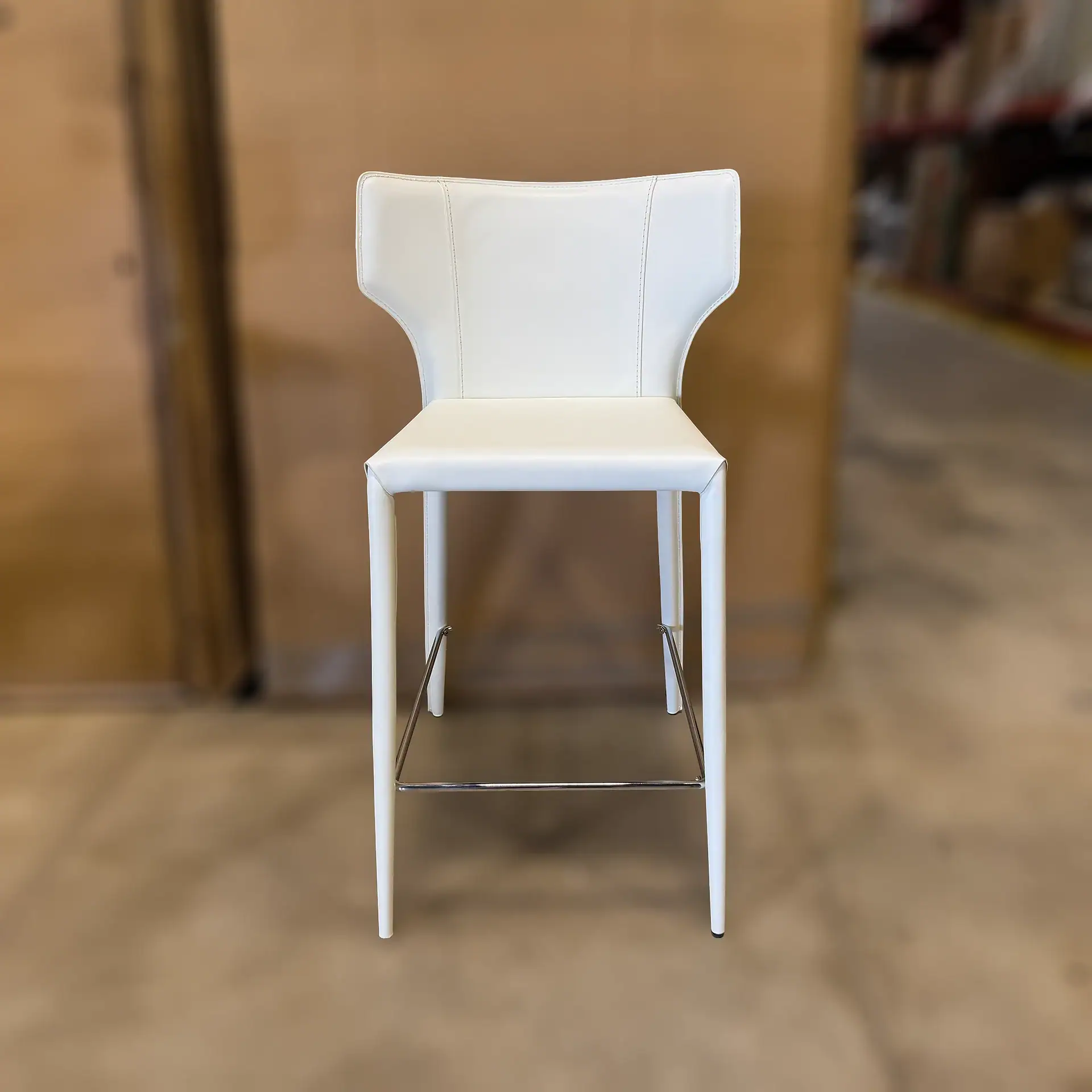 Nuevo Wayne bar stool with white upholstery and metal footrest in a showroom.