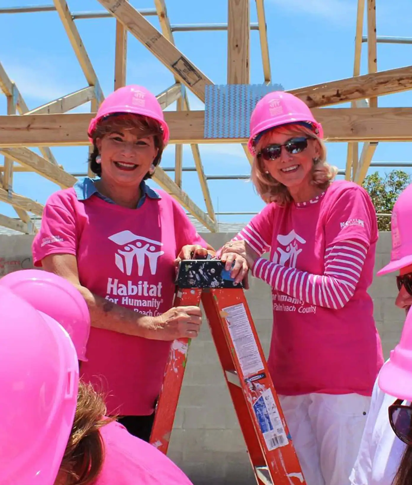 Two women in pink Habitat for Humanity shirts and helmets at a construction site.