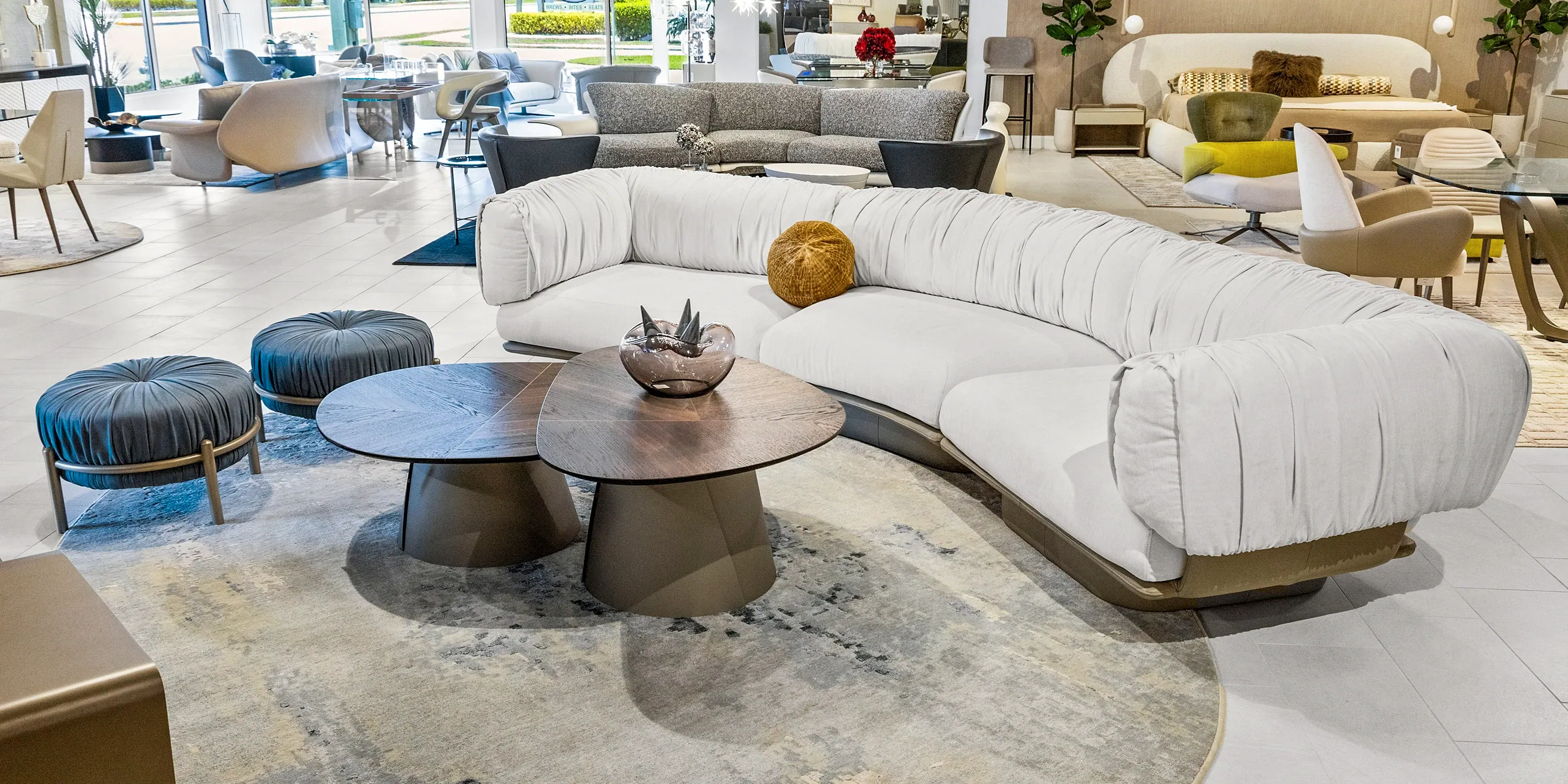 showroom-vignette-jun-26-living-room-4 White modern curved sofa with matching ottomans in a bright living room.