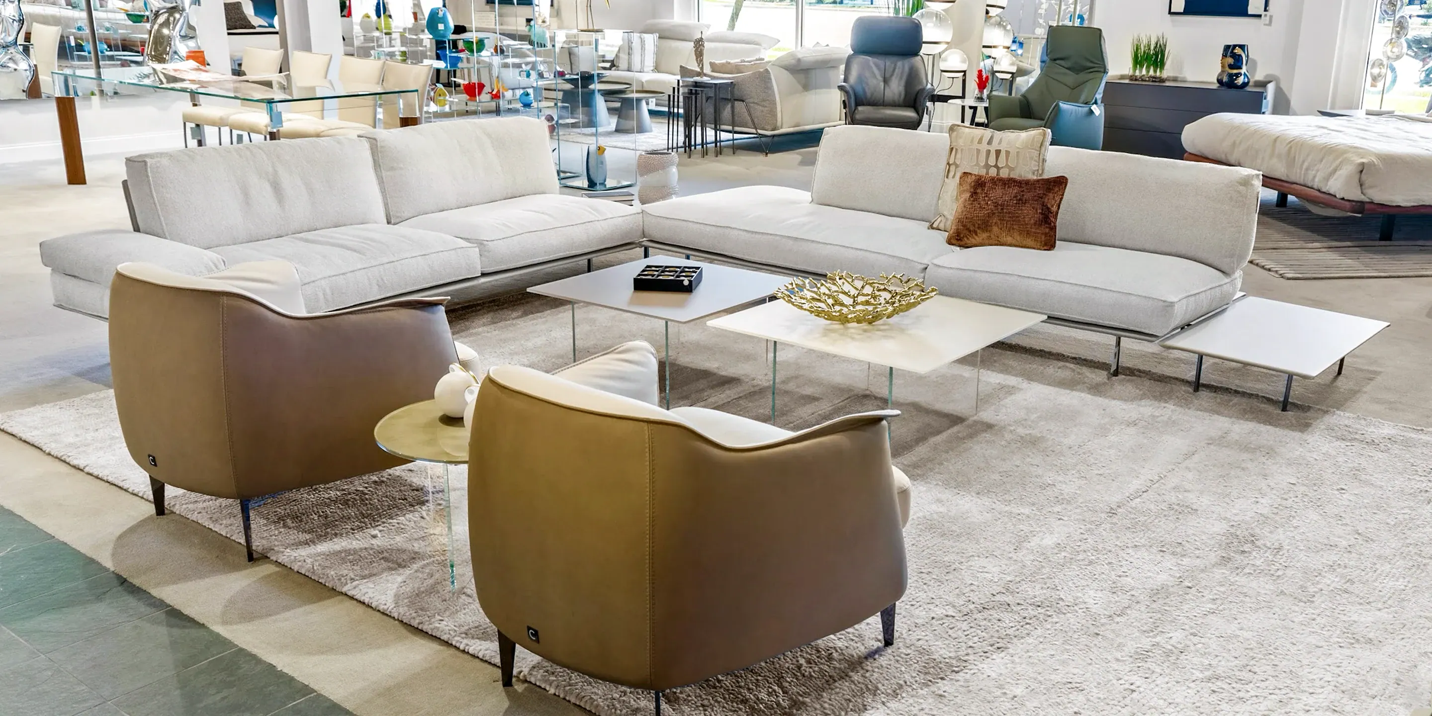 showroom-vignette-jun-26-living-room-5 Modern white sectional sofa with brown accent pillows in a bright showroom.