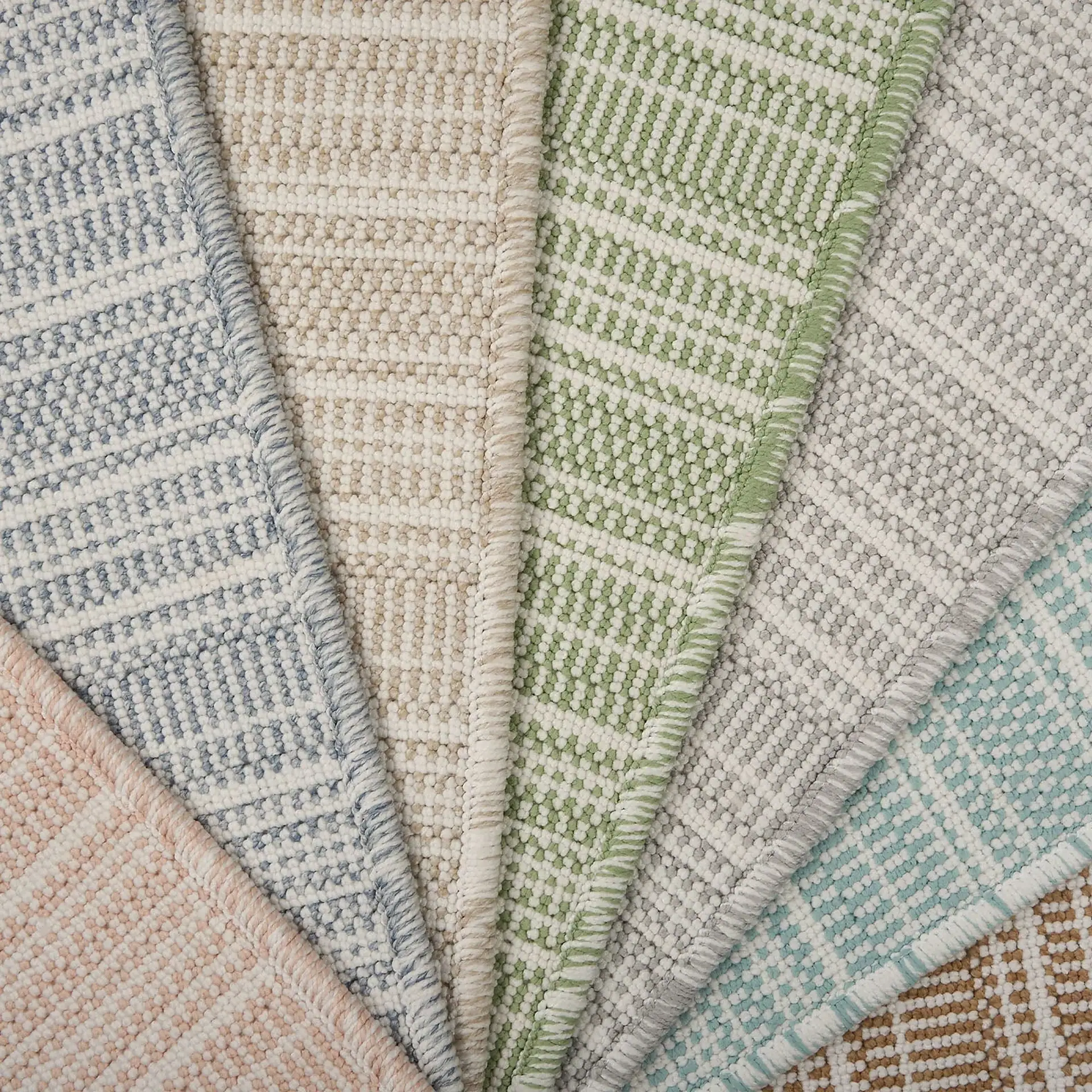 Colorful rug samples with geometric patterns in various shades of blue, green, beige, and pink.