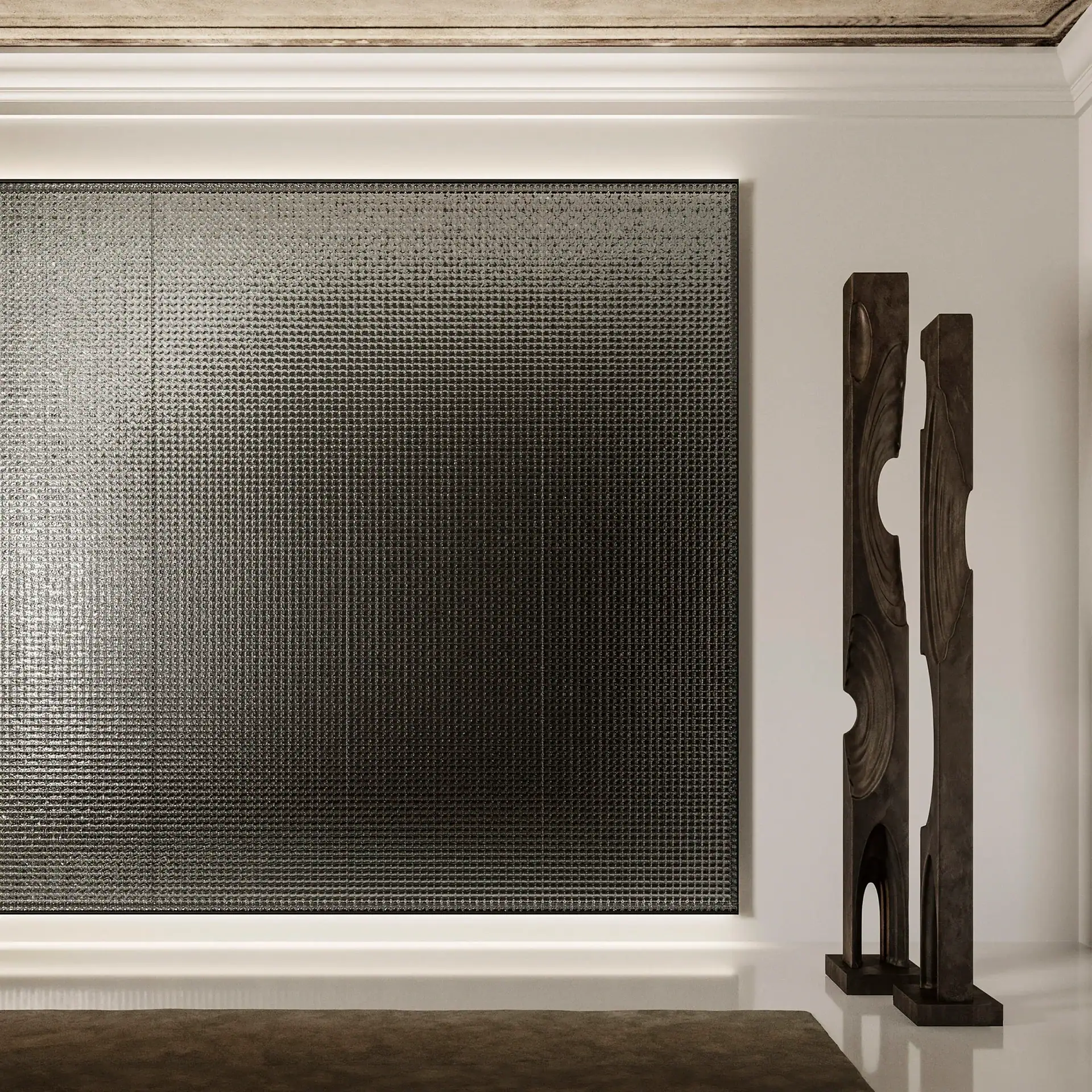 A modern room with a large, dark gray, textured art panel on a white wall, illuminated by hidden lights. Two tall, dark, abstract sculptures stand to the right, and a dark rug is on the floor.
