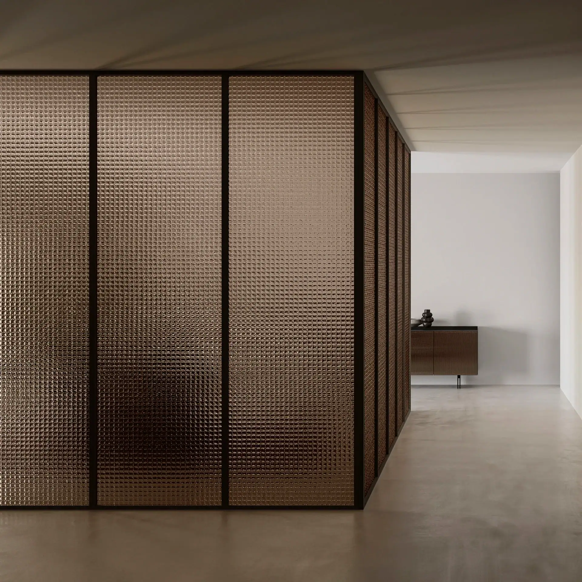 An L-shaped room divider made of dark amber textured glass panels with black frames. A concrete floor and a dark wooden cabinet with a decorative object are visible in the background.