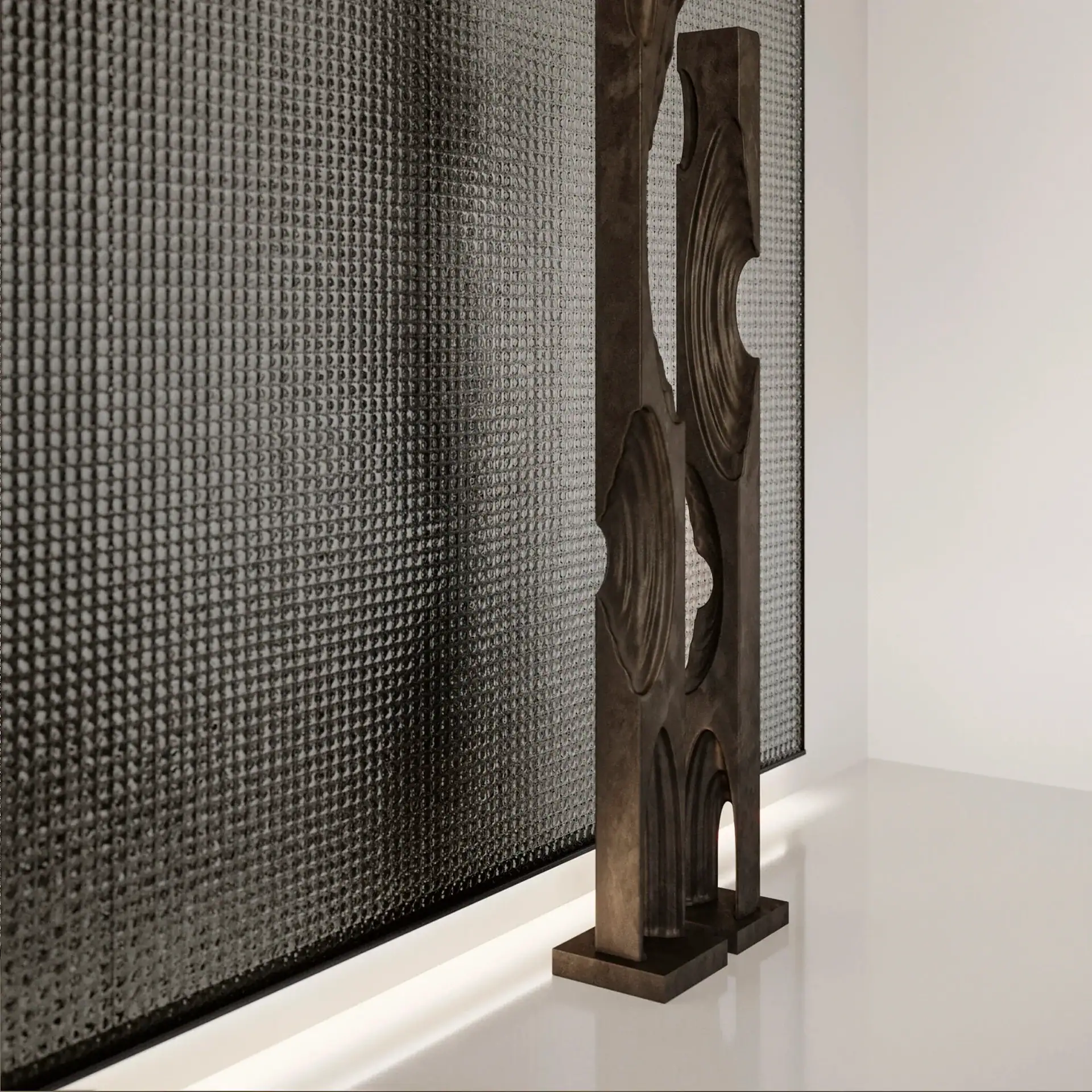 A tall, dark, sculptural room divider with organic cut-outs and internal lighting stands before a dark, textured, grid-patterned panel in a modern, white-walled room.