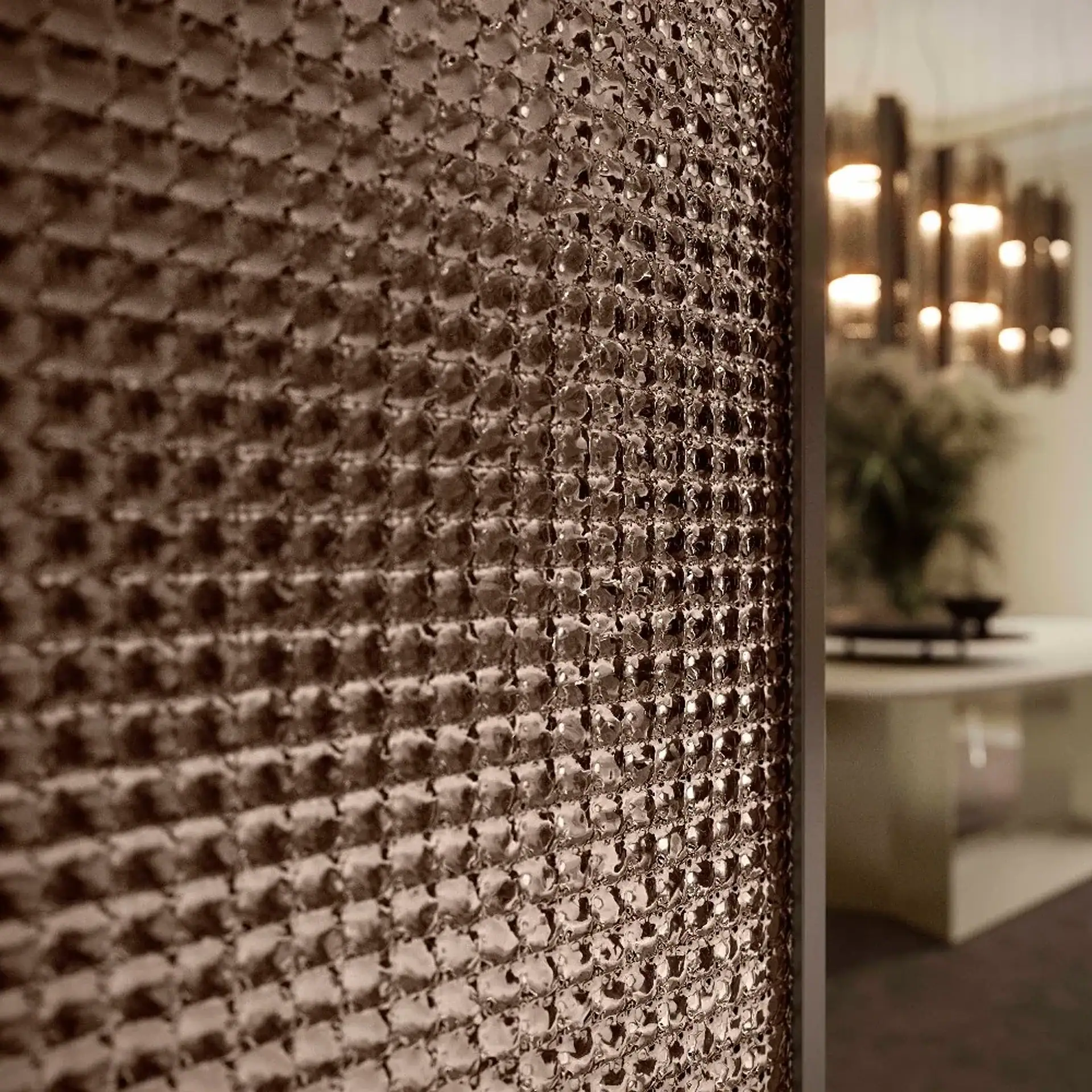 Close-up of a textured, coppery-brown panel with a grid of rounded squares, blurring a modern light fixture and room in the background.