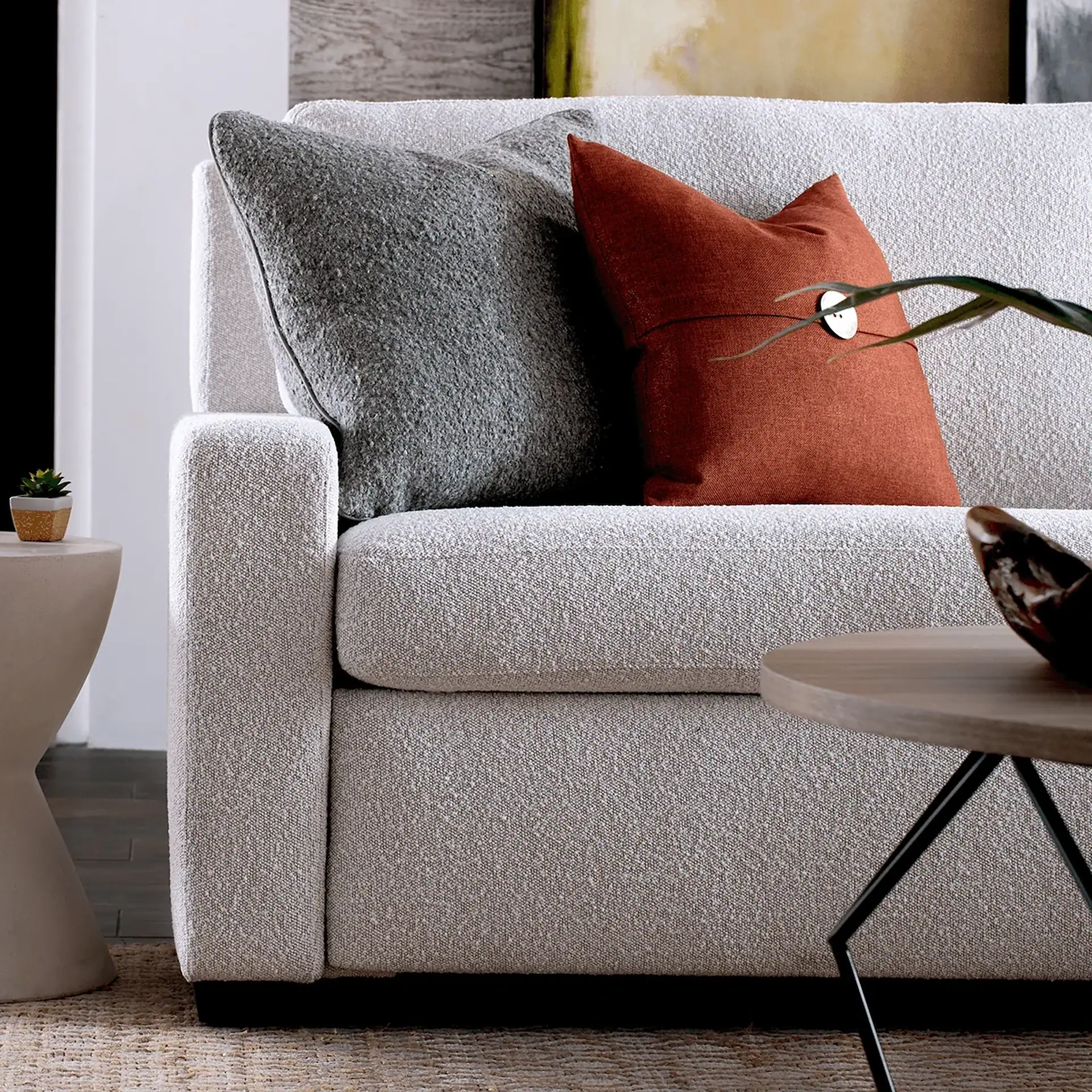 A light beige textured sofa with gray and rust-orange pillows, a side table with a succulent, and a wooden coffee table in a modern living room.