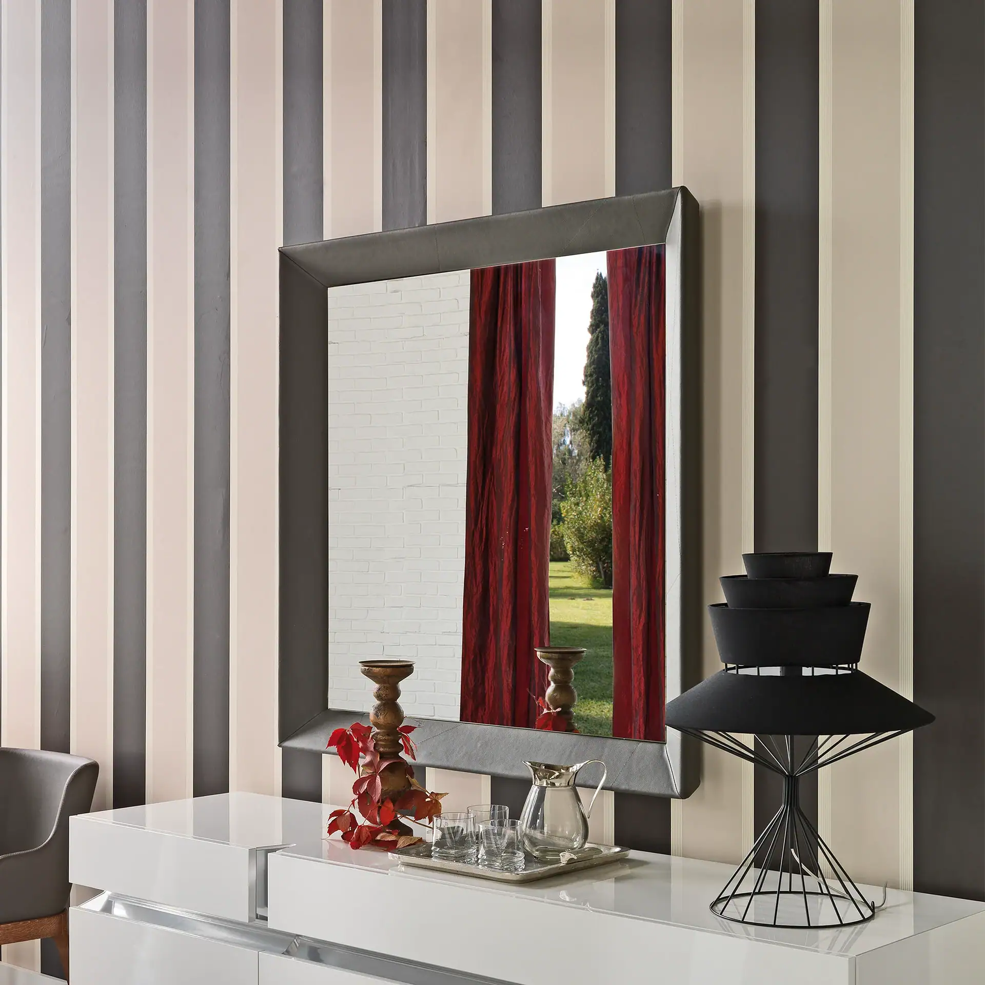 Modern wall mirror with red curtains and decorative items on white console table.