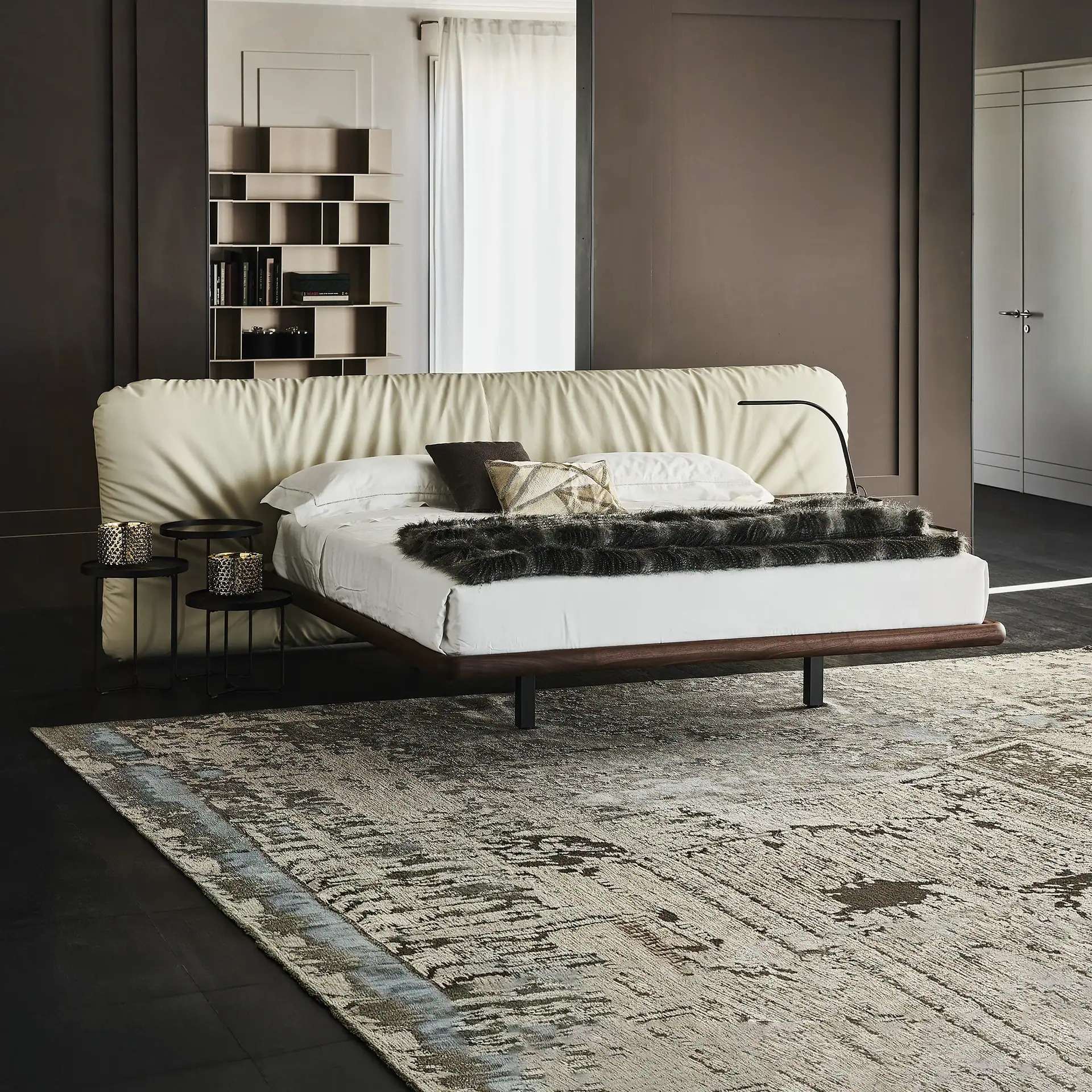 A modern bedroom with a cream upholstered bed, dark wood frame, black nightstands, and an abstract rug on a dark floor.