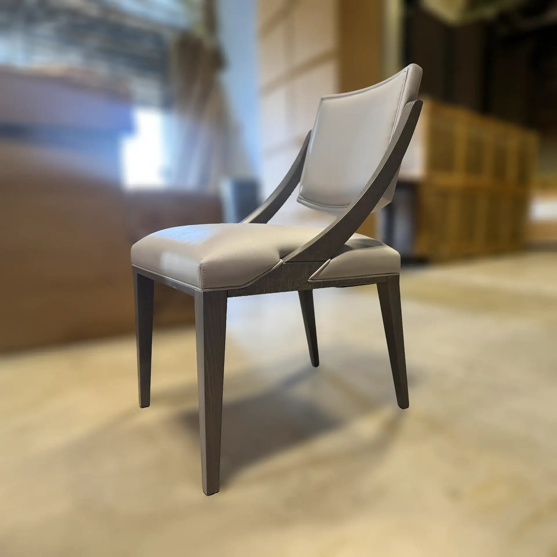 A modern dining chair with light grey upholstery and a dark wood frame, viewed from an angle on a light floor.
