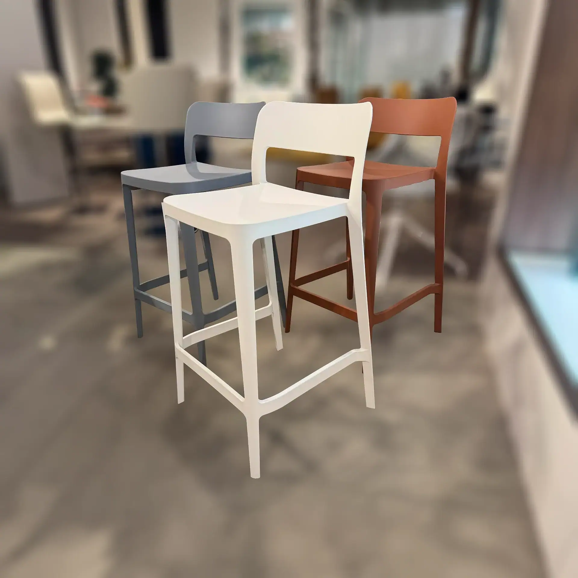 Three modern bar stools in white, grey, and terracotta colors, arranged on a light brown floor.