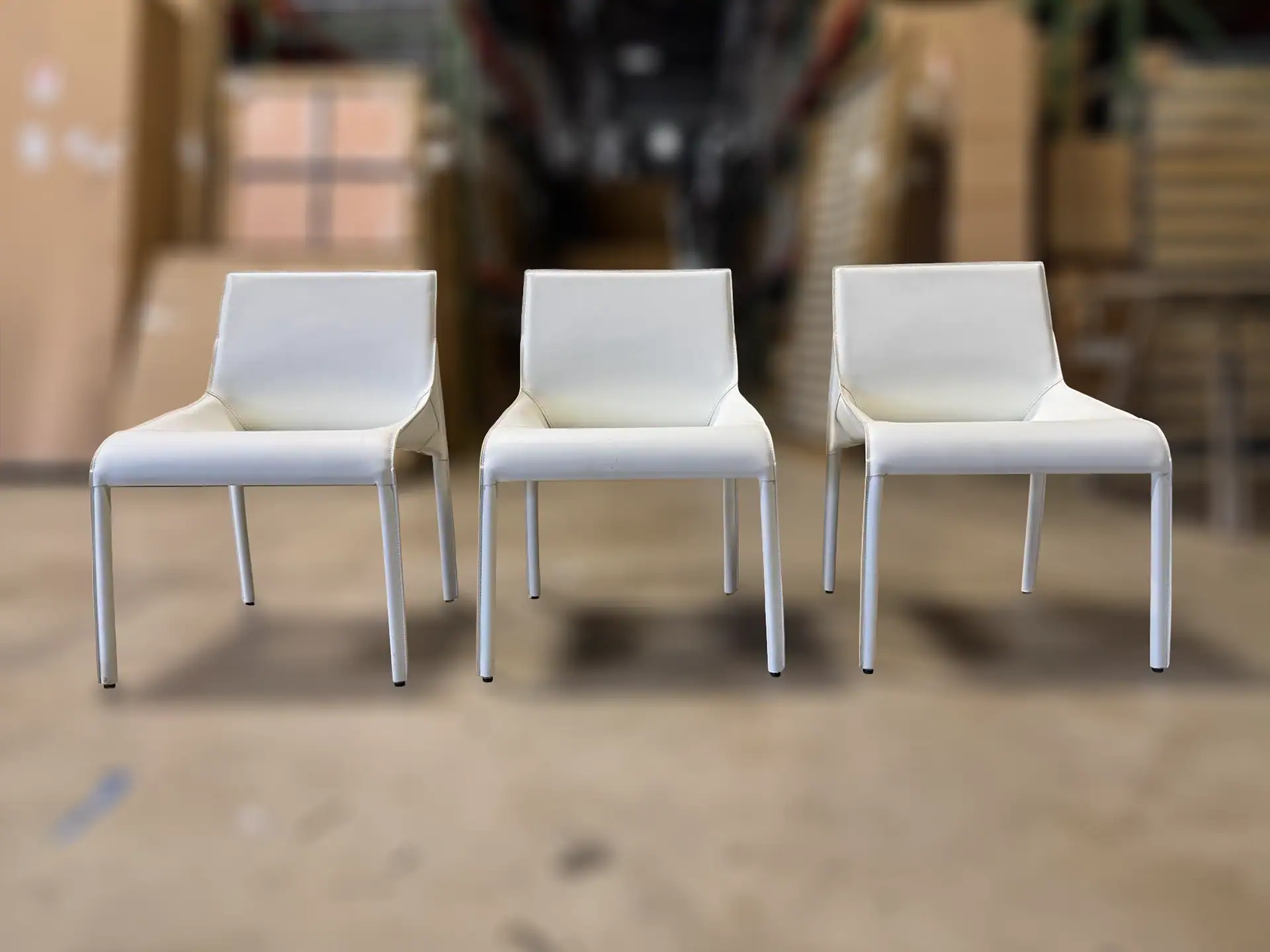 Three white Nuevo Colter dining chairs in a furniture store.