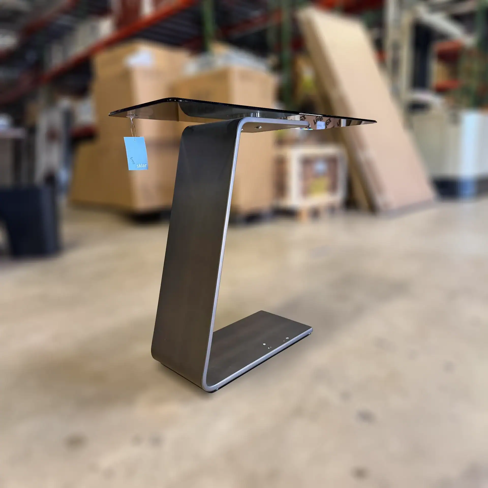 Reflex OH console table with black glass top and metal base in warehouse setting.