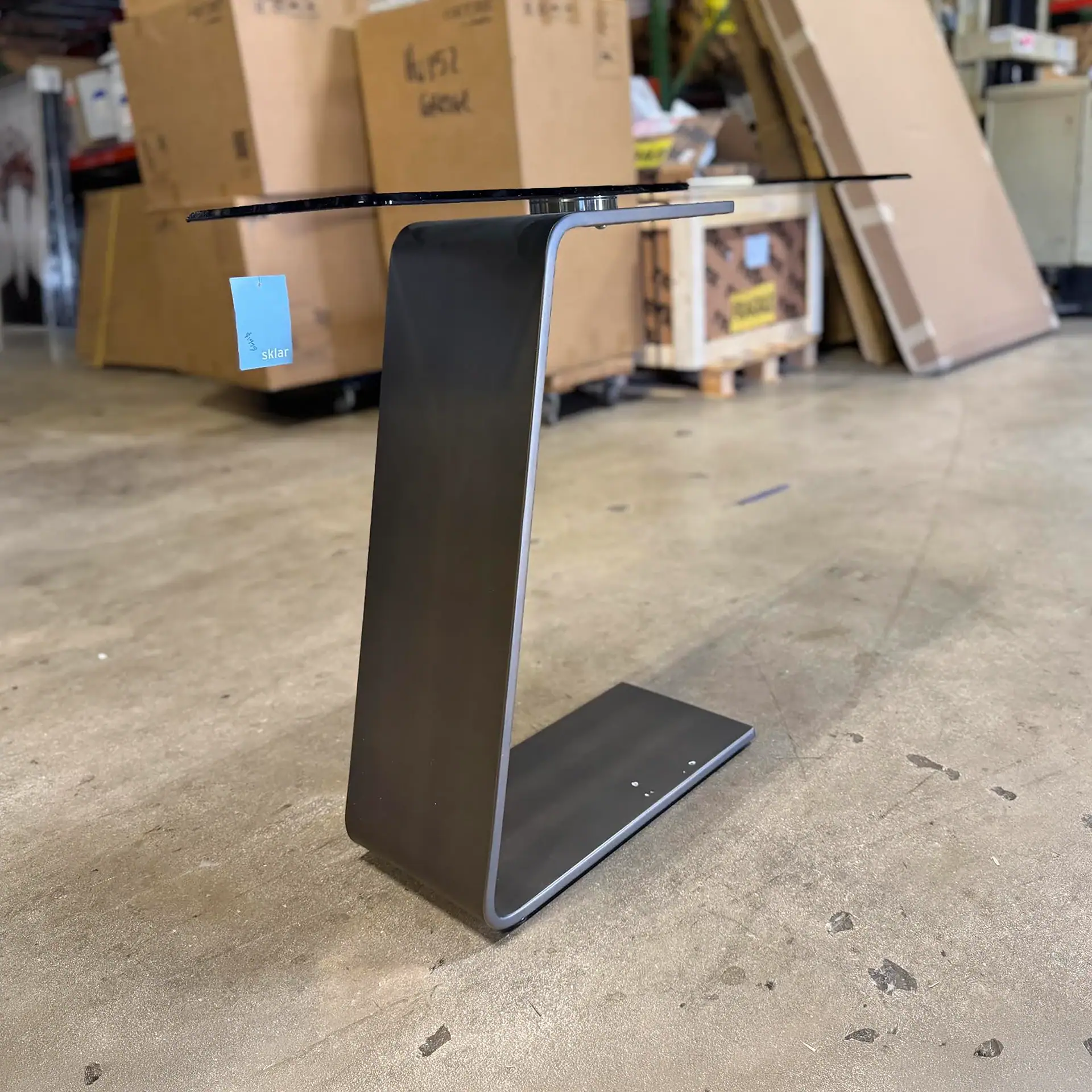 Reflex OH console table with glass top and metal base in a warehouse setting.