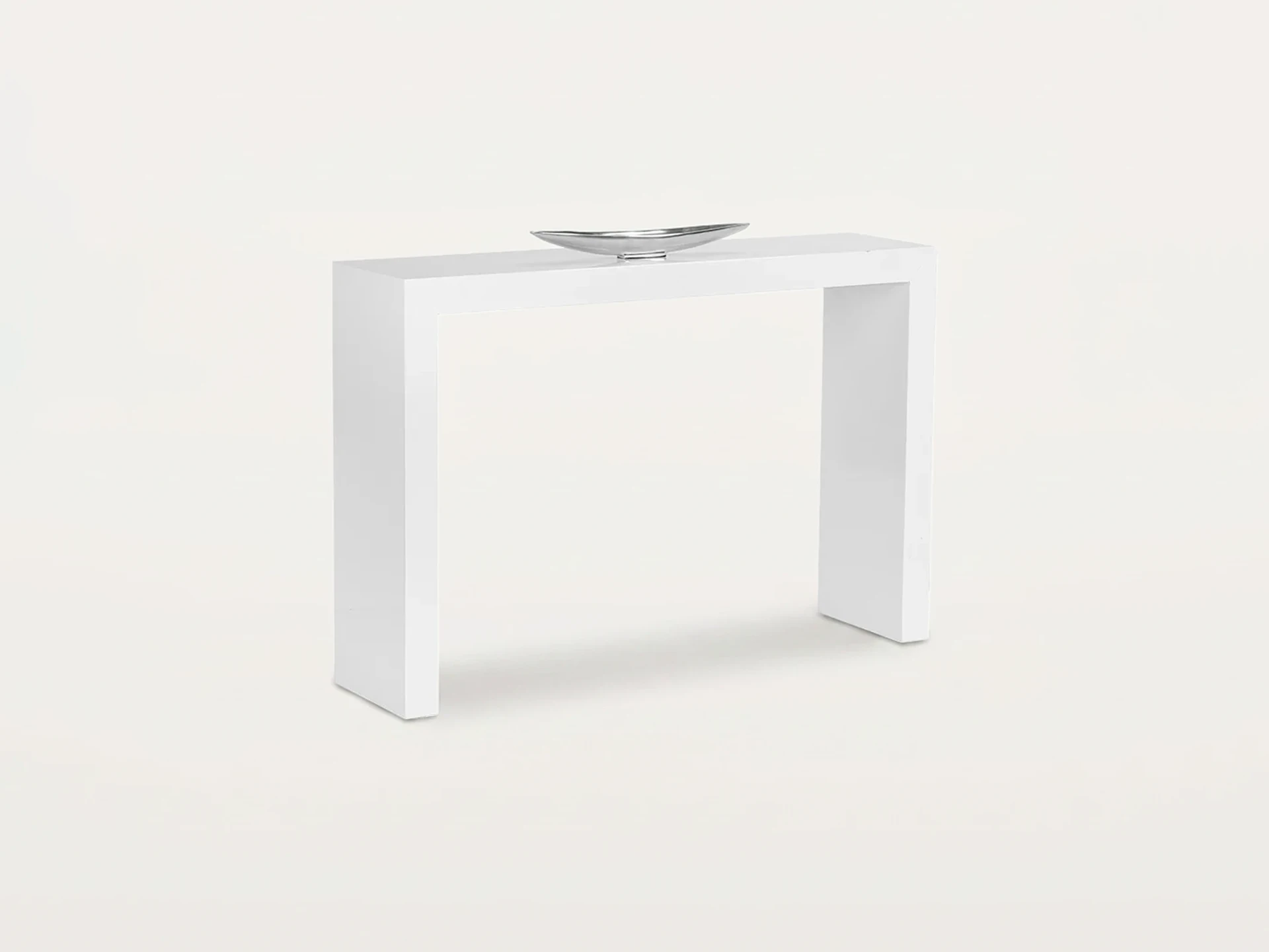 A white minimalist console table with a silver, elongated decorative bowl on top, set against a light background.