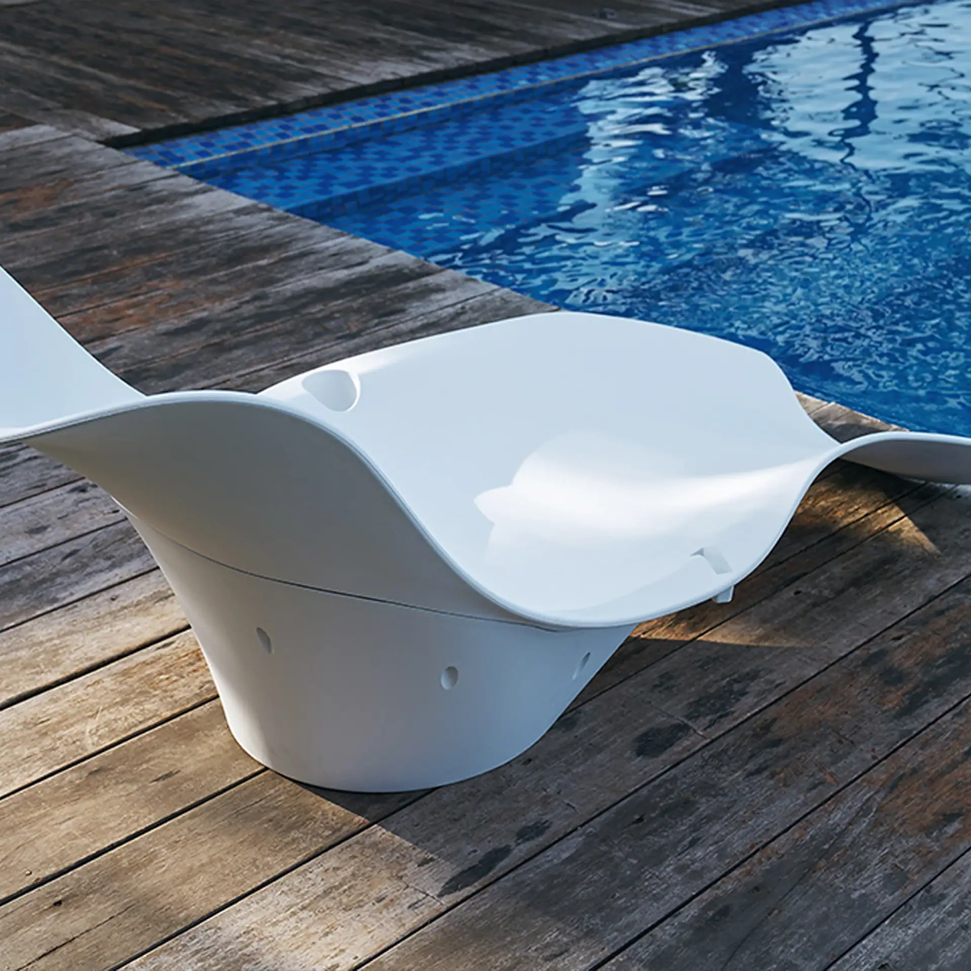 A modern white lounge chair with a wave-like design sits on a weathered wooden deck next to a blue swimming pool.