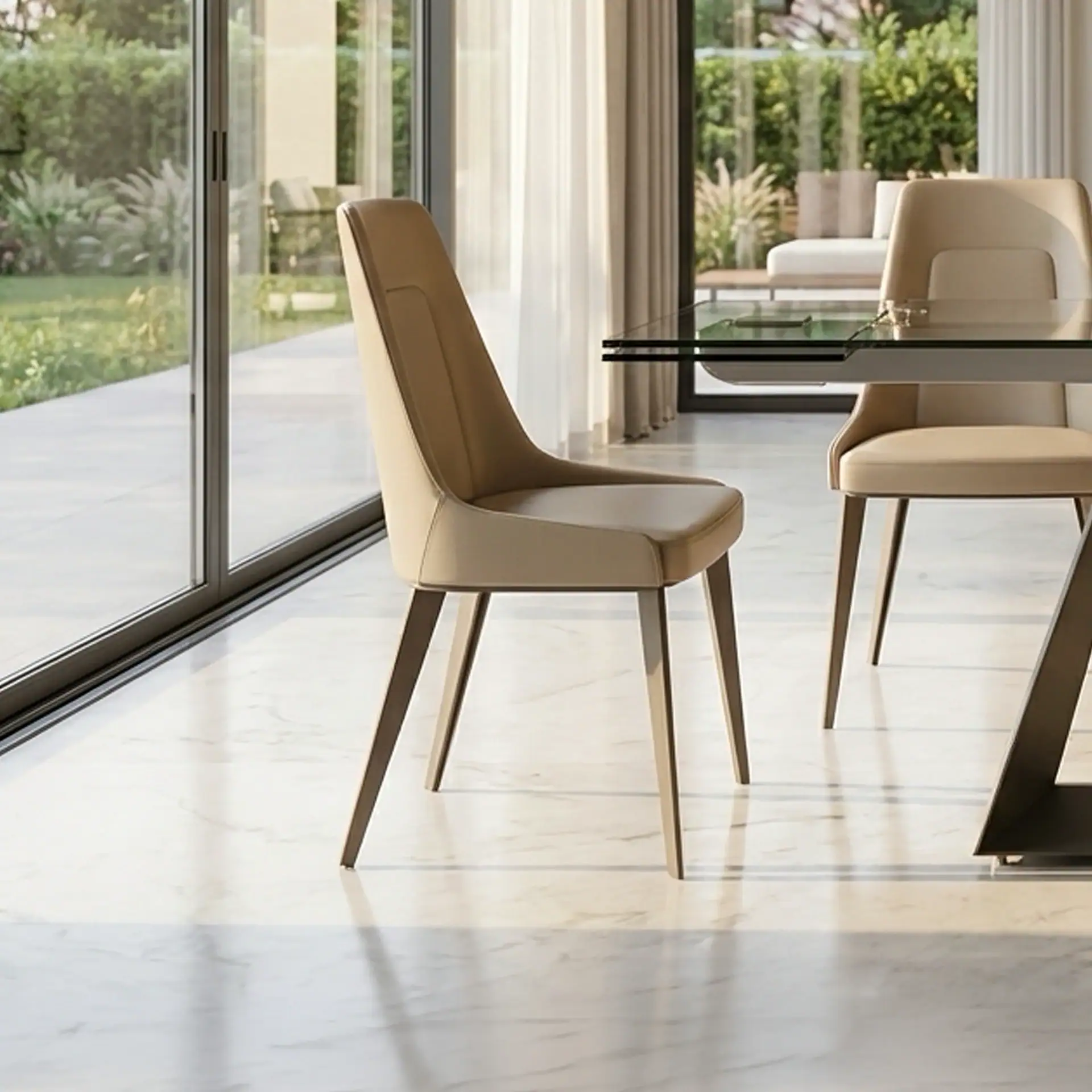 Two beige dining chairs and a glass-top table in a modern room with large sliding glass doors overlooking a green garden.