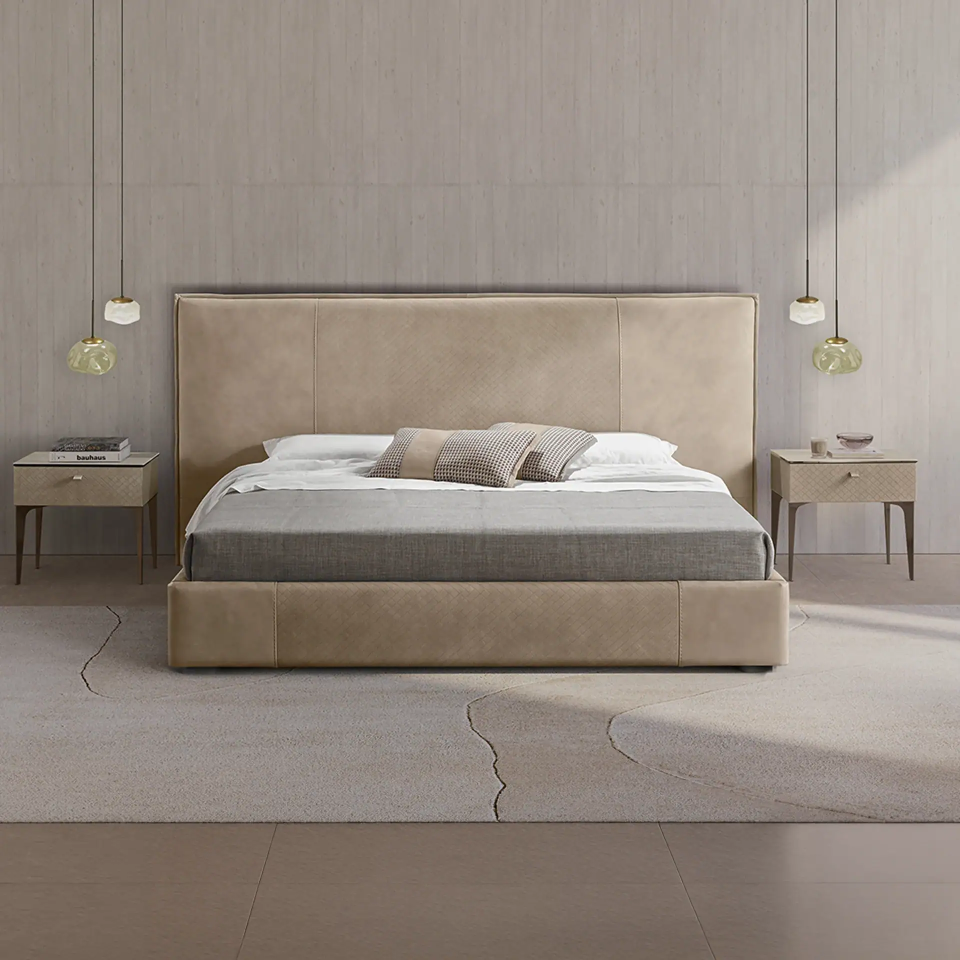 A modern bedroom with a large beige upholstered bed, two matching nightstands, and unique pendant lights. The bed has white and grey bedding with patterned pillows. A light-colored rug with an abstract design covers a wooden floor.