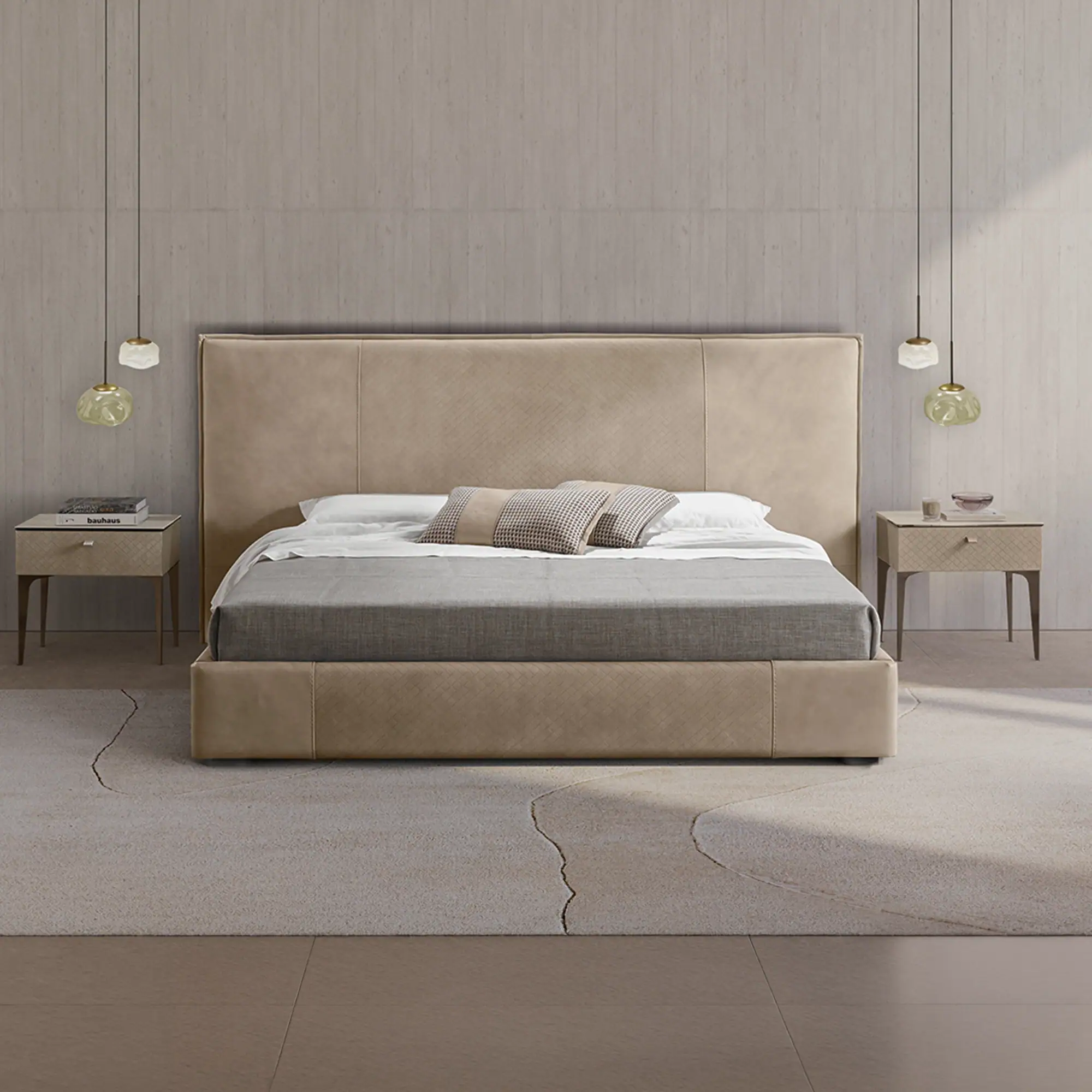 A modern bedroom with a large beige upholstered bed, two matching nightstands, and unique pendant lights. The bed has white and grey bedding with patterned pillows. A light-colored rug with an abstract design covers a wooden floor.