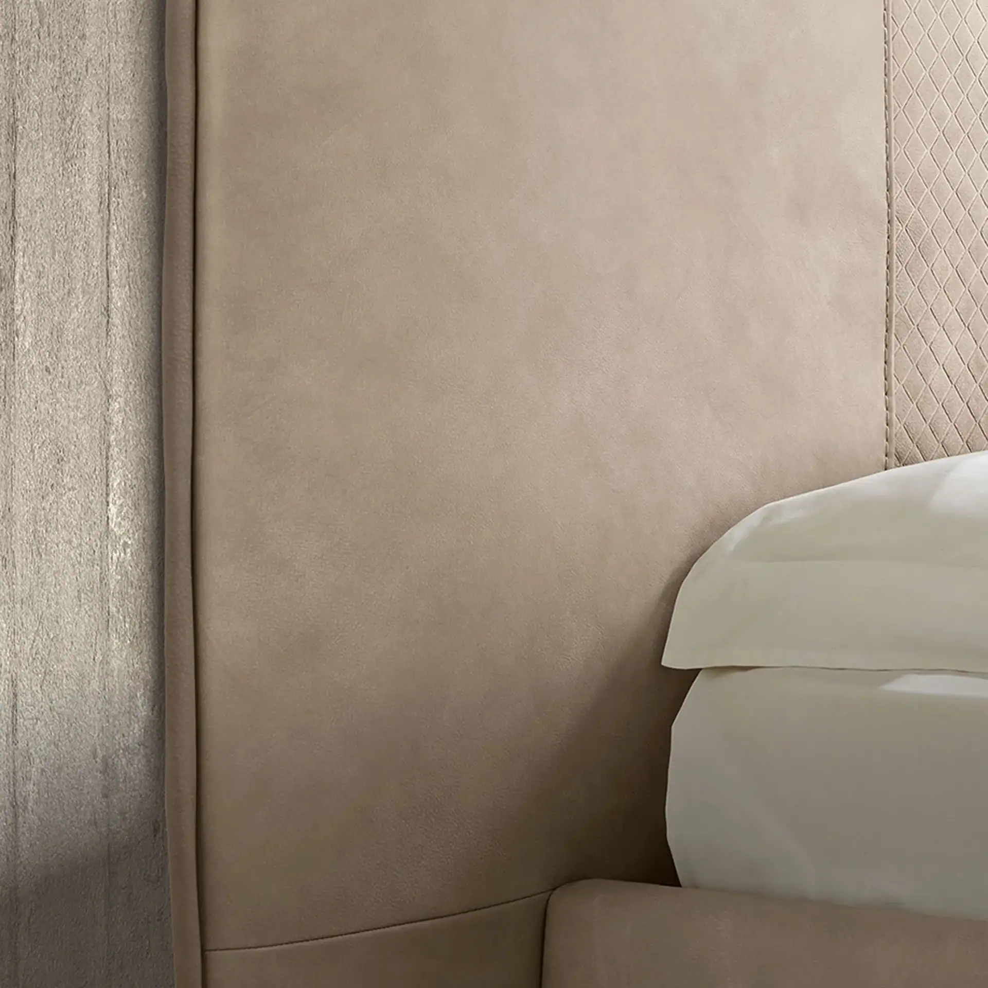 Close-up of a beige upholstered headboard with smooth and diamond-patterned sections, next to a textured wall and white bedding.
