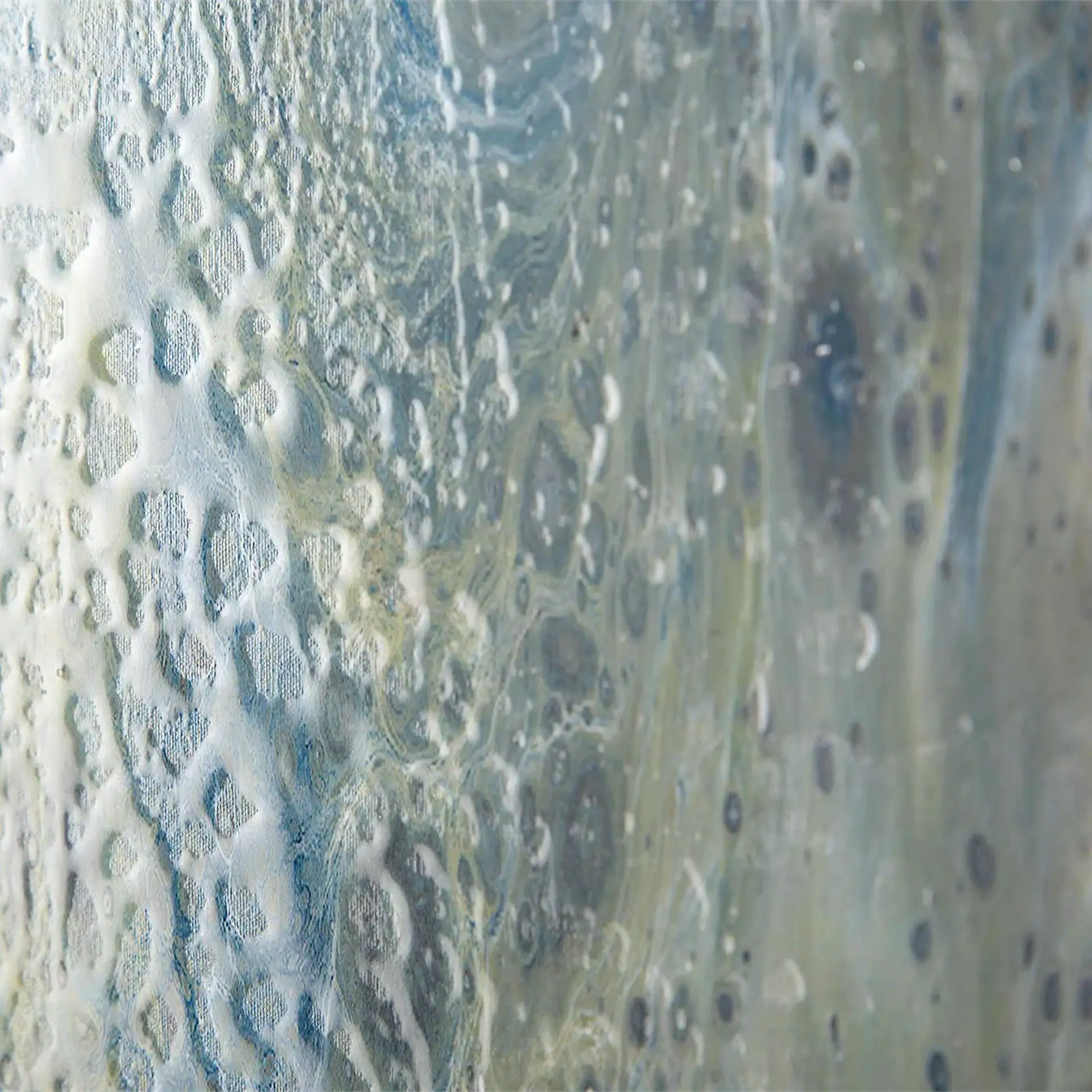 Abstract close-up of a textured surface with white and light blue raised patterns on the left, transitioning to smoother blue, gray, and yellow swirls with dark circular shapes on the right.