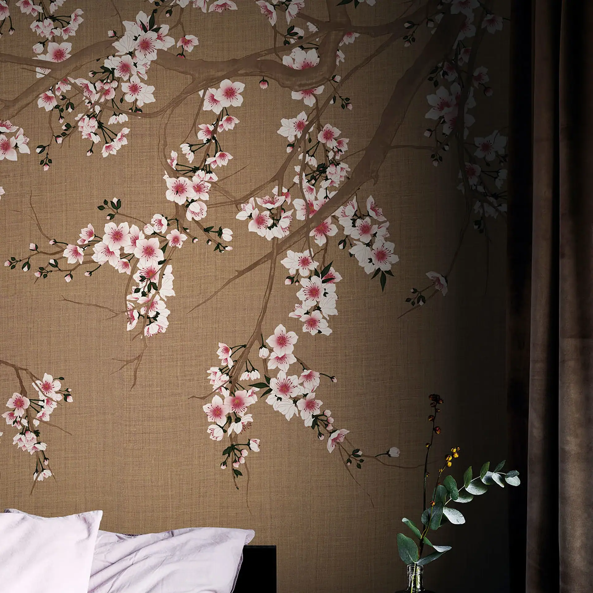 A bedroom wall with textured brown wallpaper featuring white and pink cherry blossoms, next to a bed with purple bedding and a vase with eucalyptus.