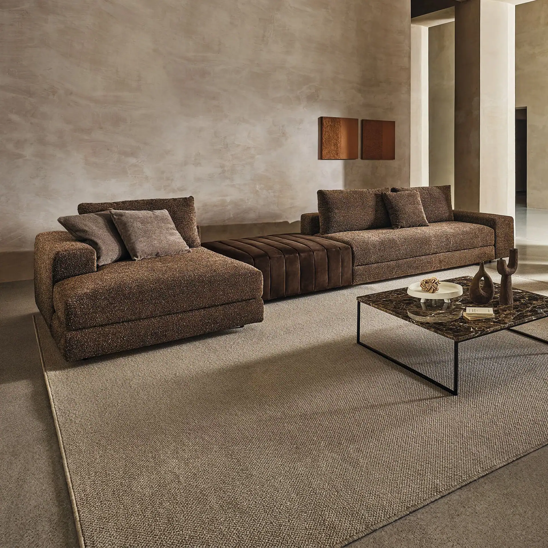 A modern living room with a large brown sectional sofa, a marble coffee table with decor, and textured beige walls with abstract art.
