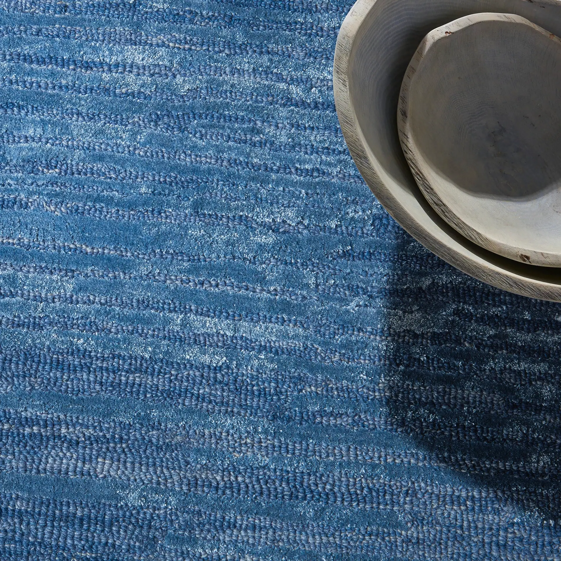 Blue textured rug with ceramic bowls on top.