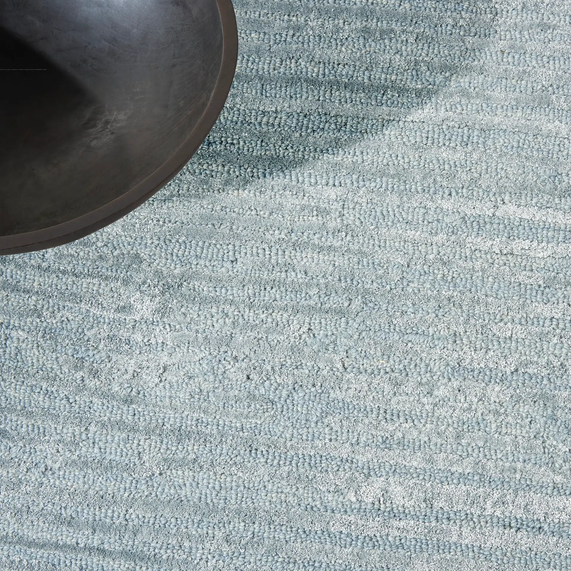 Close-up of a blue textured area rug with a black round table edge.