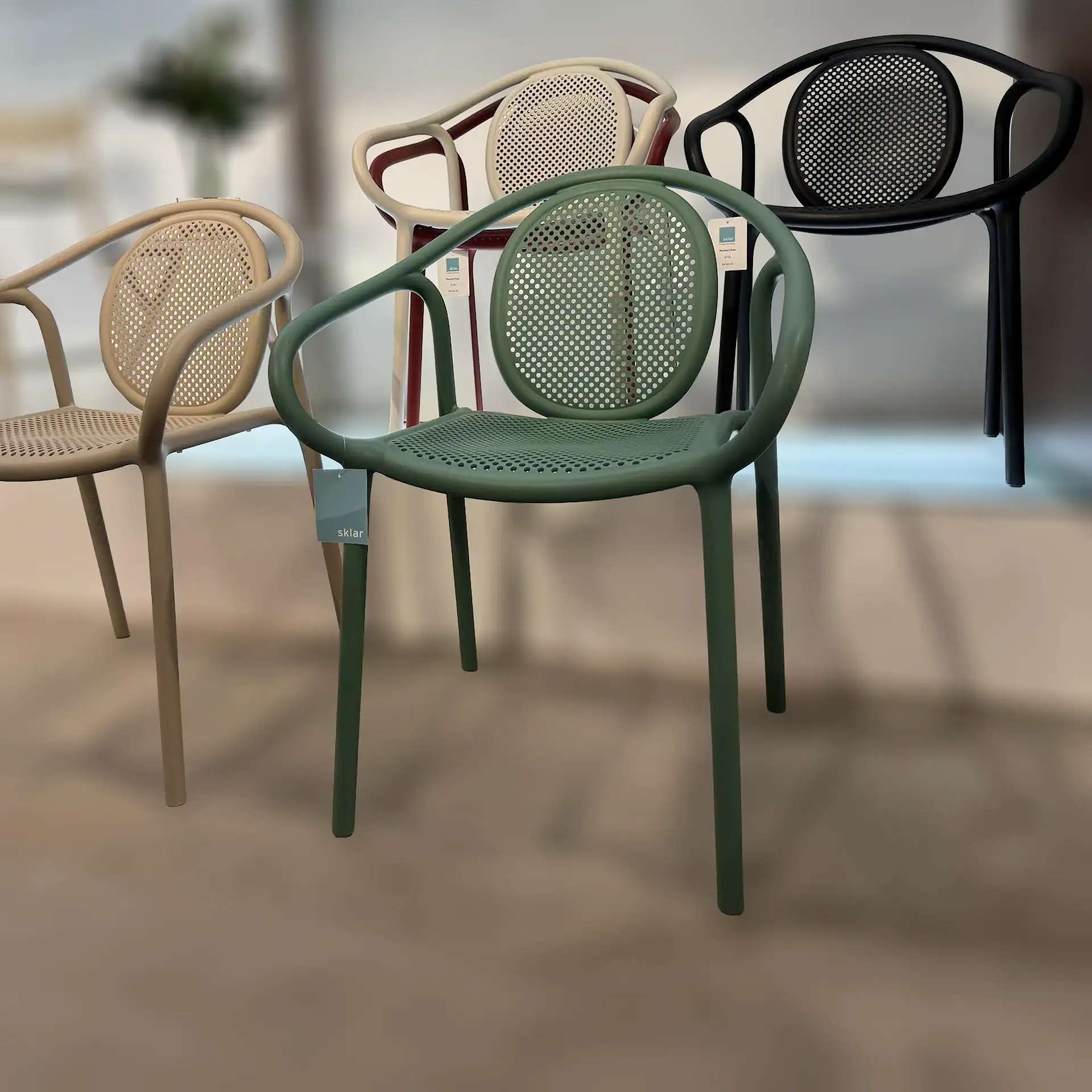 Four modern chairs in dark green, light beige, off-white, and black, featuring rounded frames and perforated seats and backrests, displayed in an indoor setting.