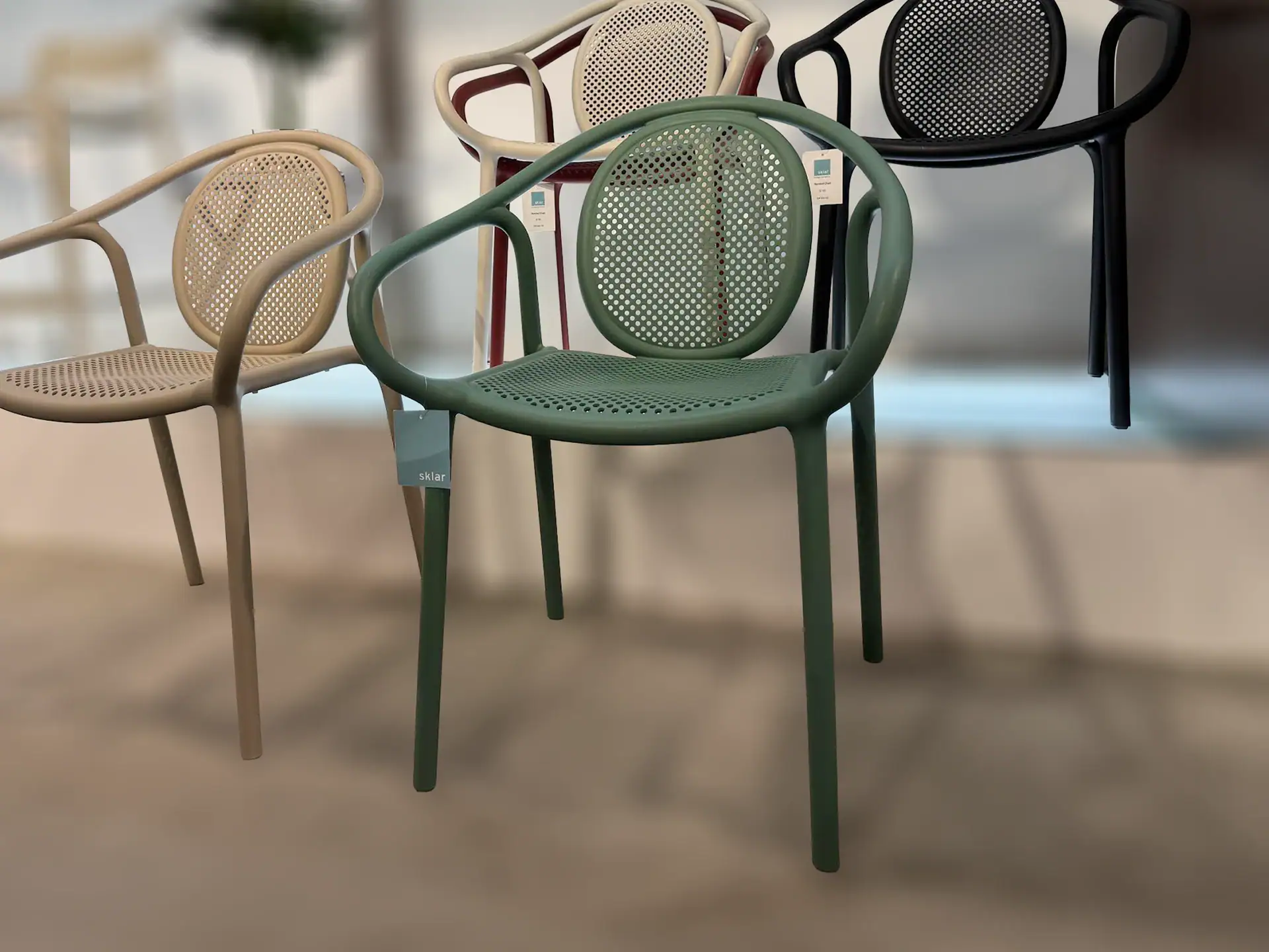 Four modern chairs with perforated seats and backs, in colors including green, beige, white with red, and black, displayed in an indoor setting.