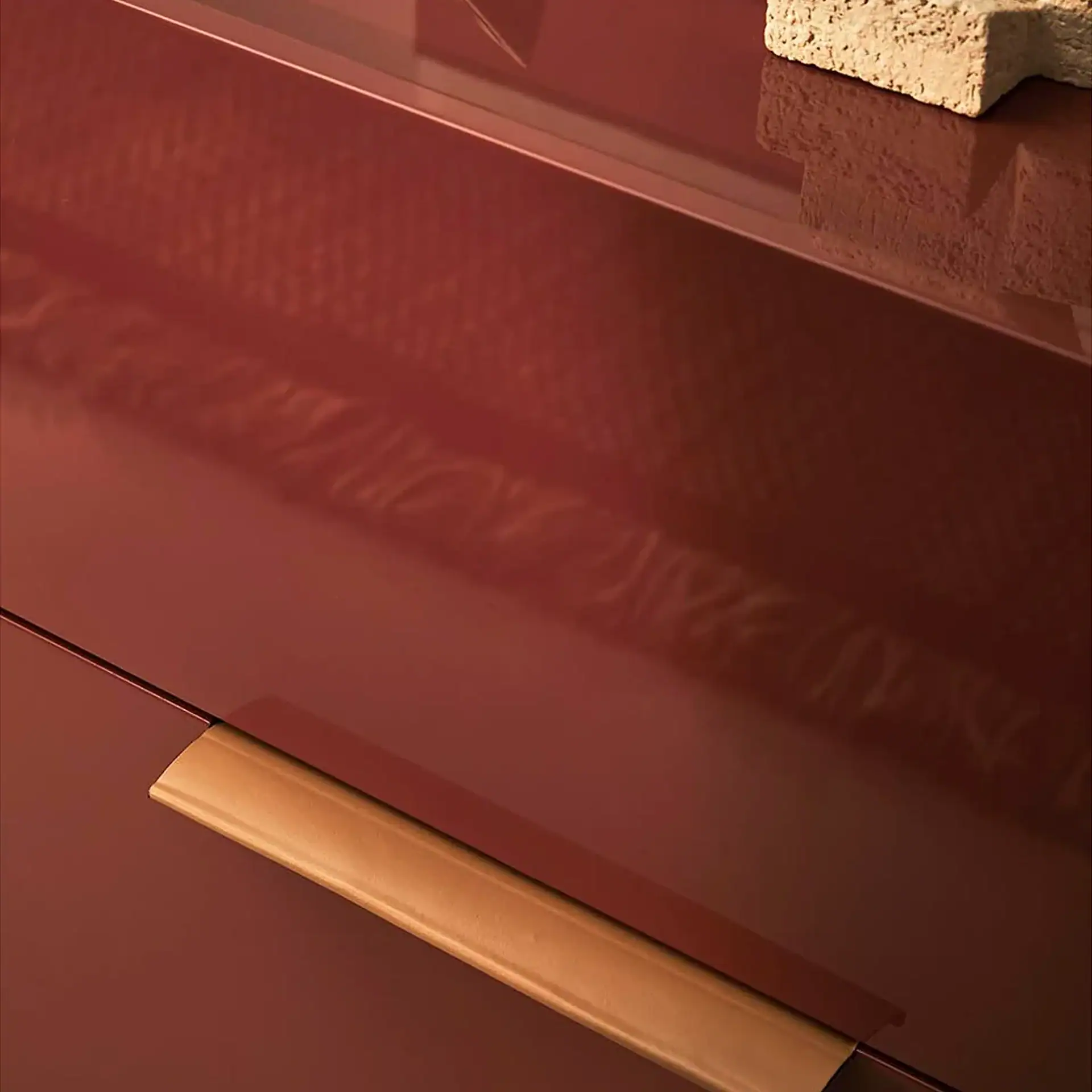 Close-up of a glossy reddish-brown surface with a light brown curved handle. A rough, light-colored object is partially visible and reflected on the surface.