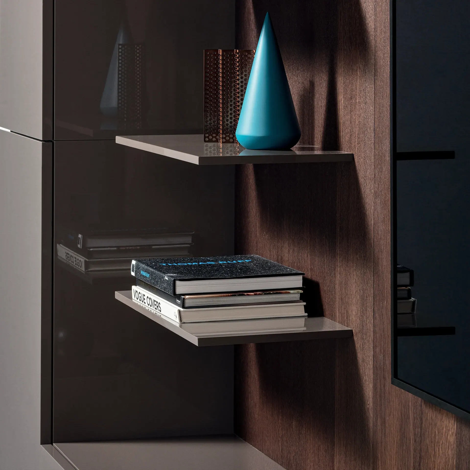 Modern shelving unit with two floating shelves. The top shelf holds a teal cone and a perforated metal screen. The bottom shelf has a stack of three books, including 'Thomas Ruff' and 'Vogue Covers'.