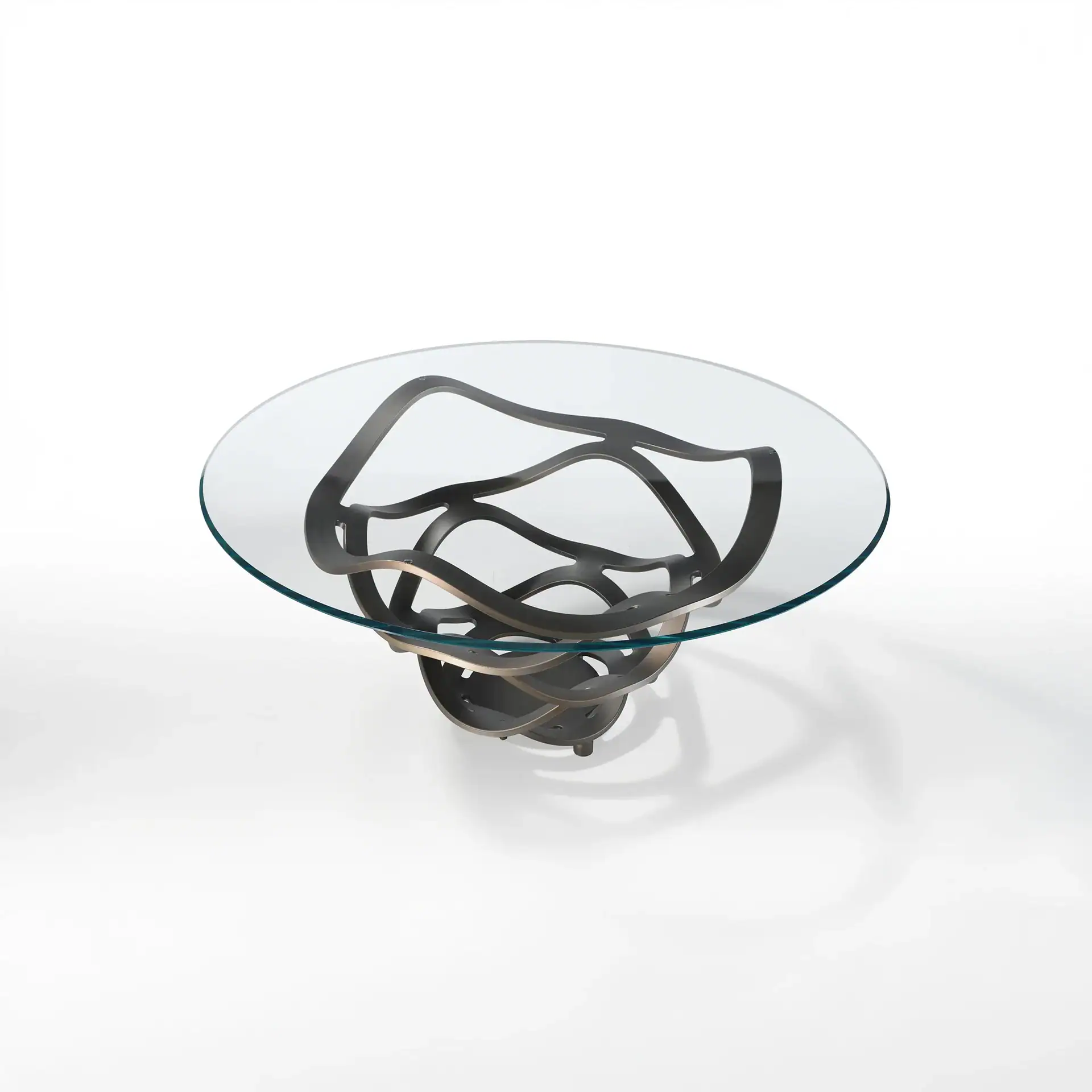 A round coffee table with a clear glass top and a dark, abstract, sculptural metal base on a white background.
