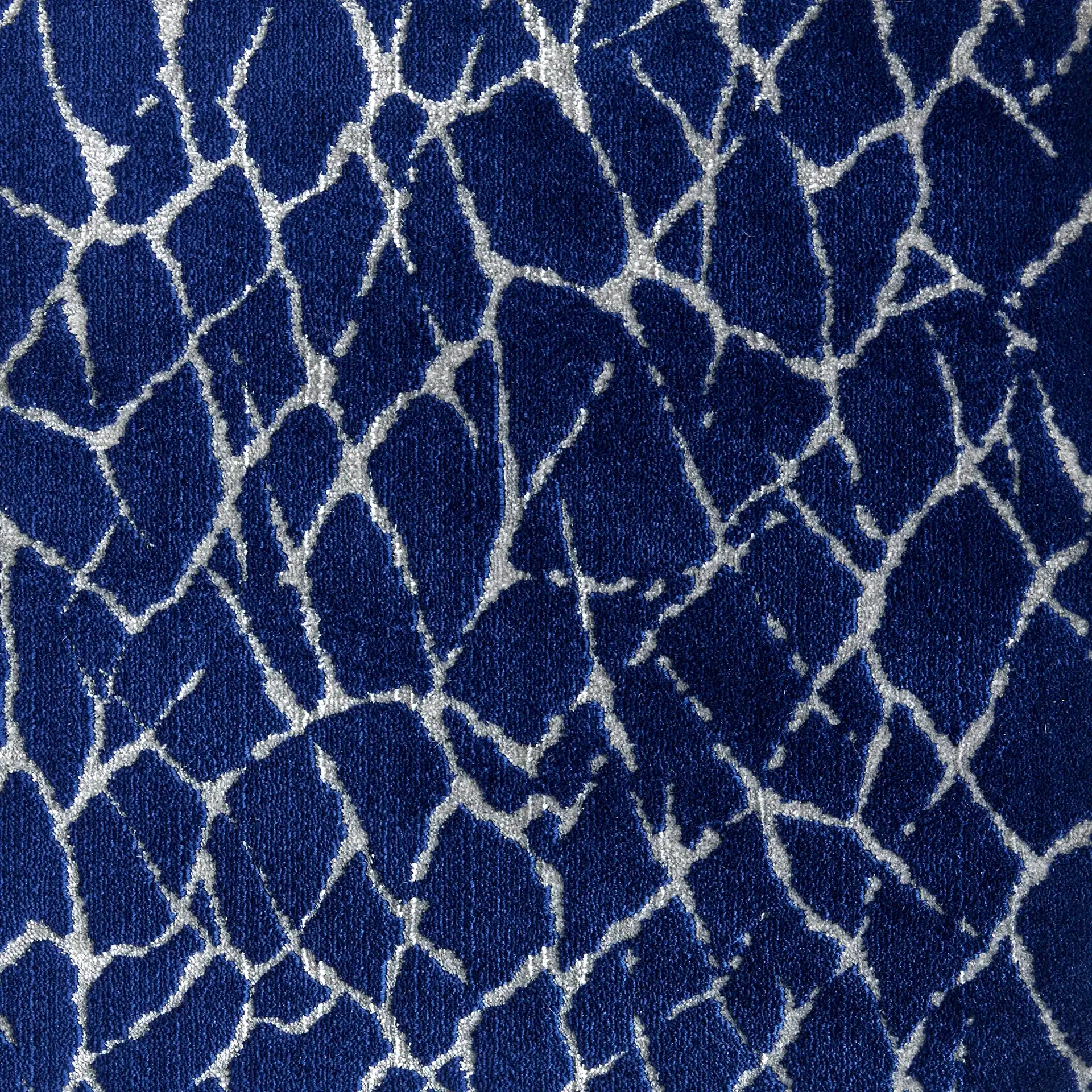 Close-up of a textured fabric with a dark blue background and an irregular, web-like pattern in silvery-gray.