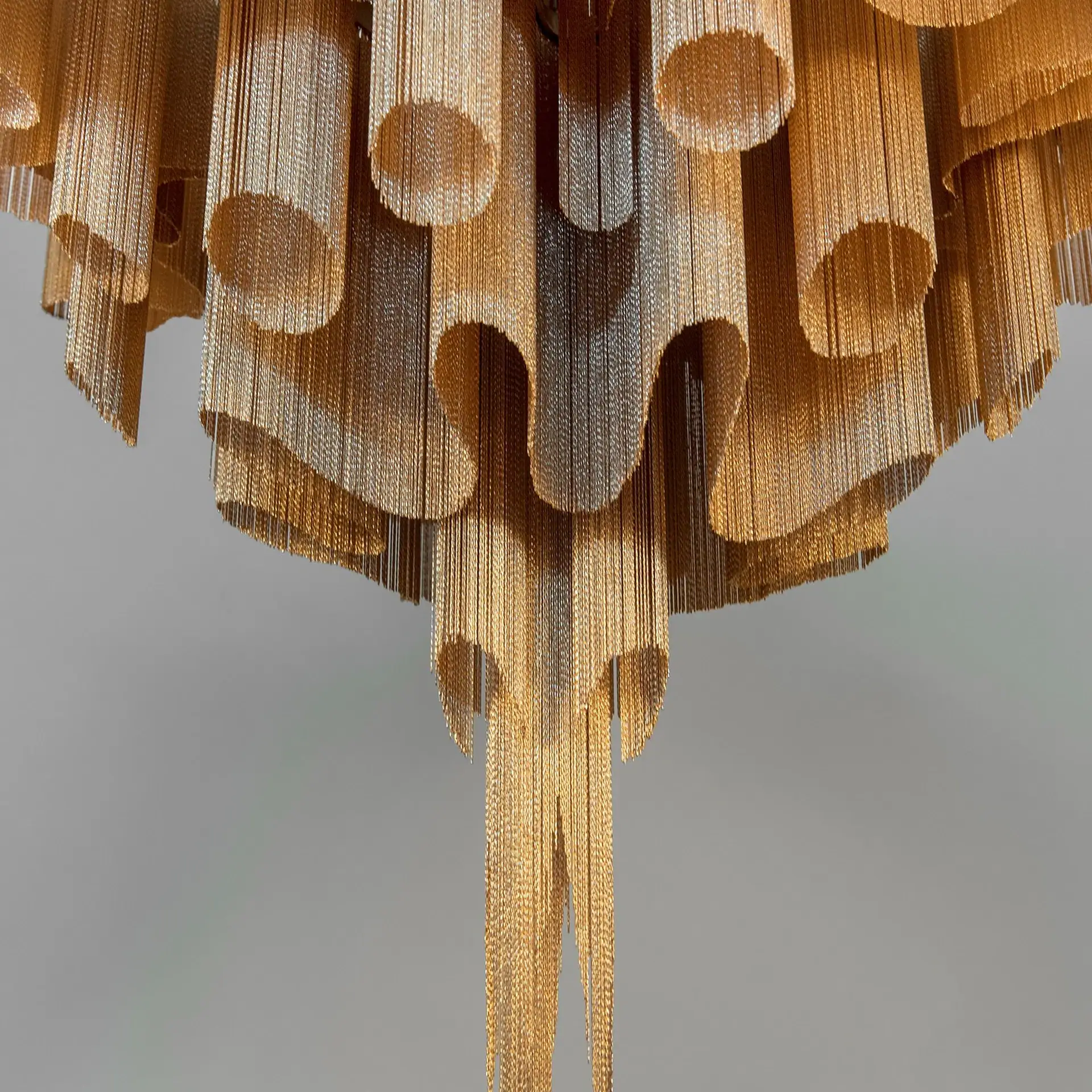 A chandelier made of golden and silver metallic chains, arranged in undulating layers and cascading forms.