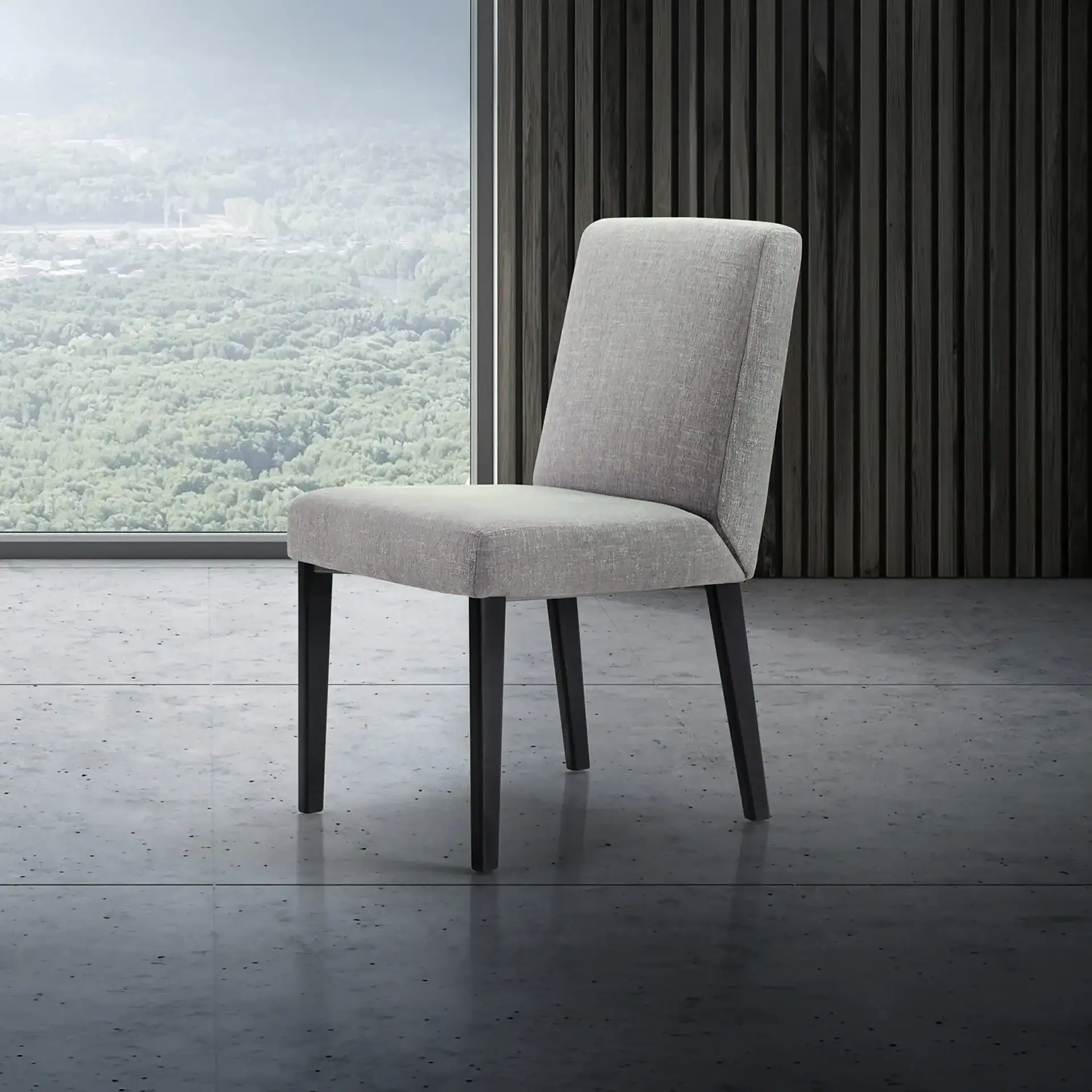 A light gray upholstered dining chair with dark legs sits on a concrete floor in a modern room with a large window overlooking a forest.