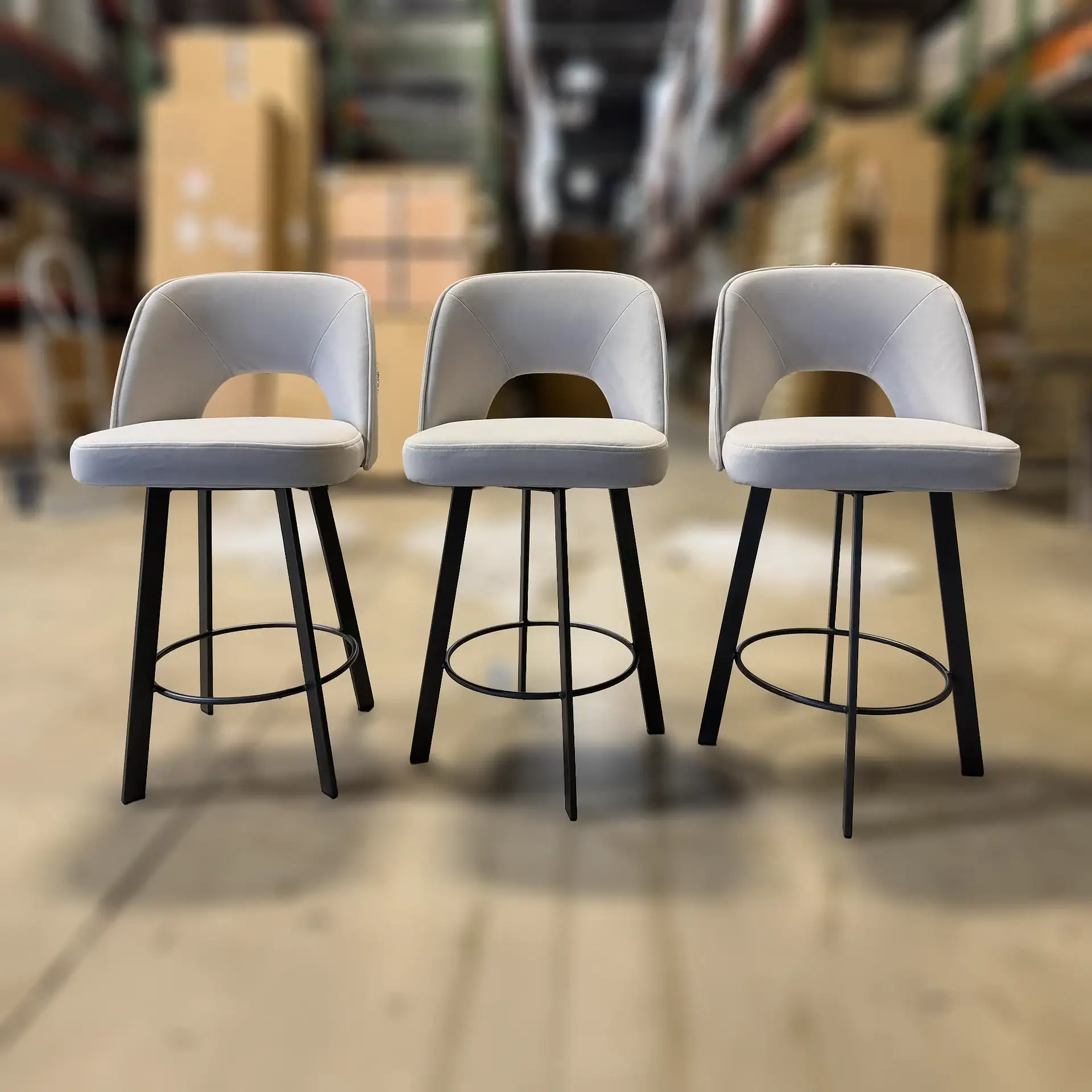 Three Trica Mia swivel counter stools with white seats and black legs in a warehouse.
