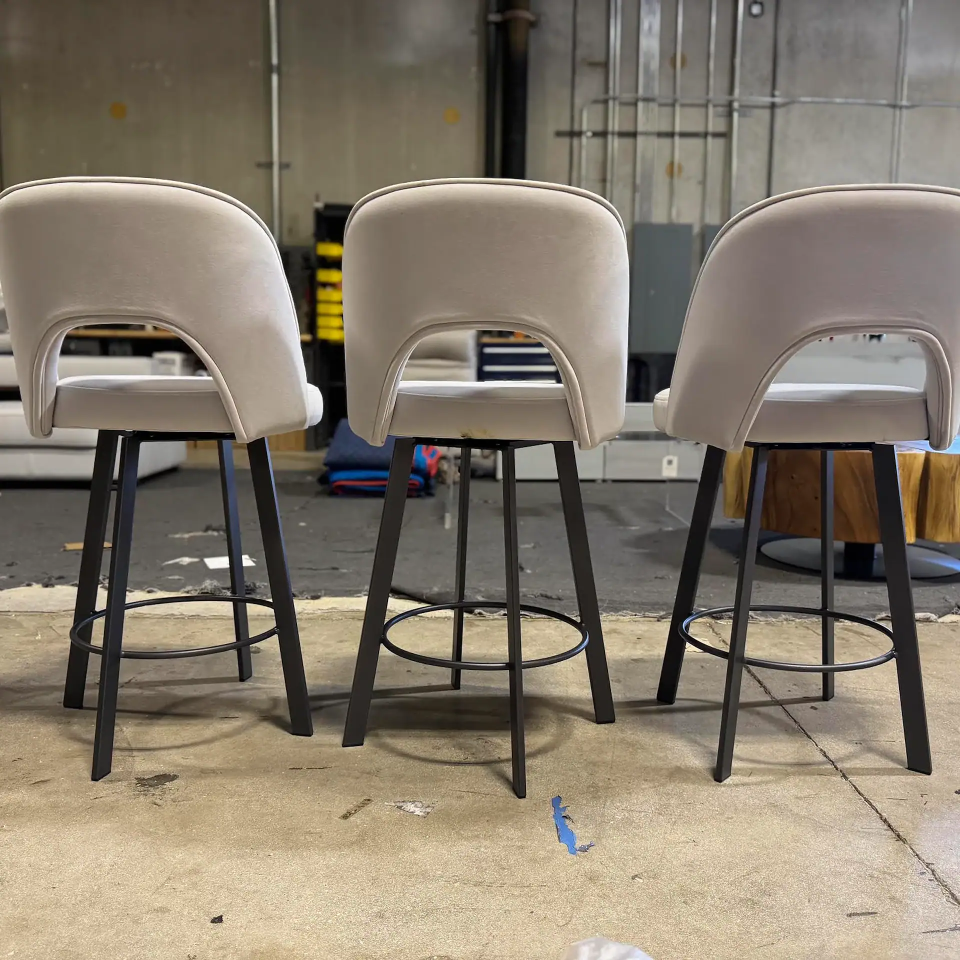 Three Trica Mia swivel counter stools with beige upholstery and black metal legs.