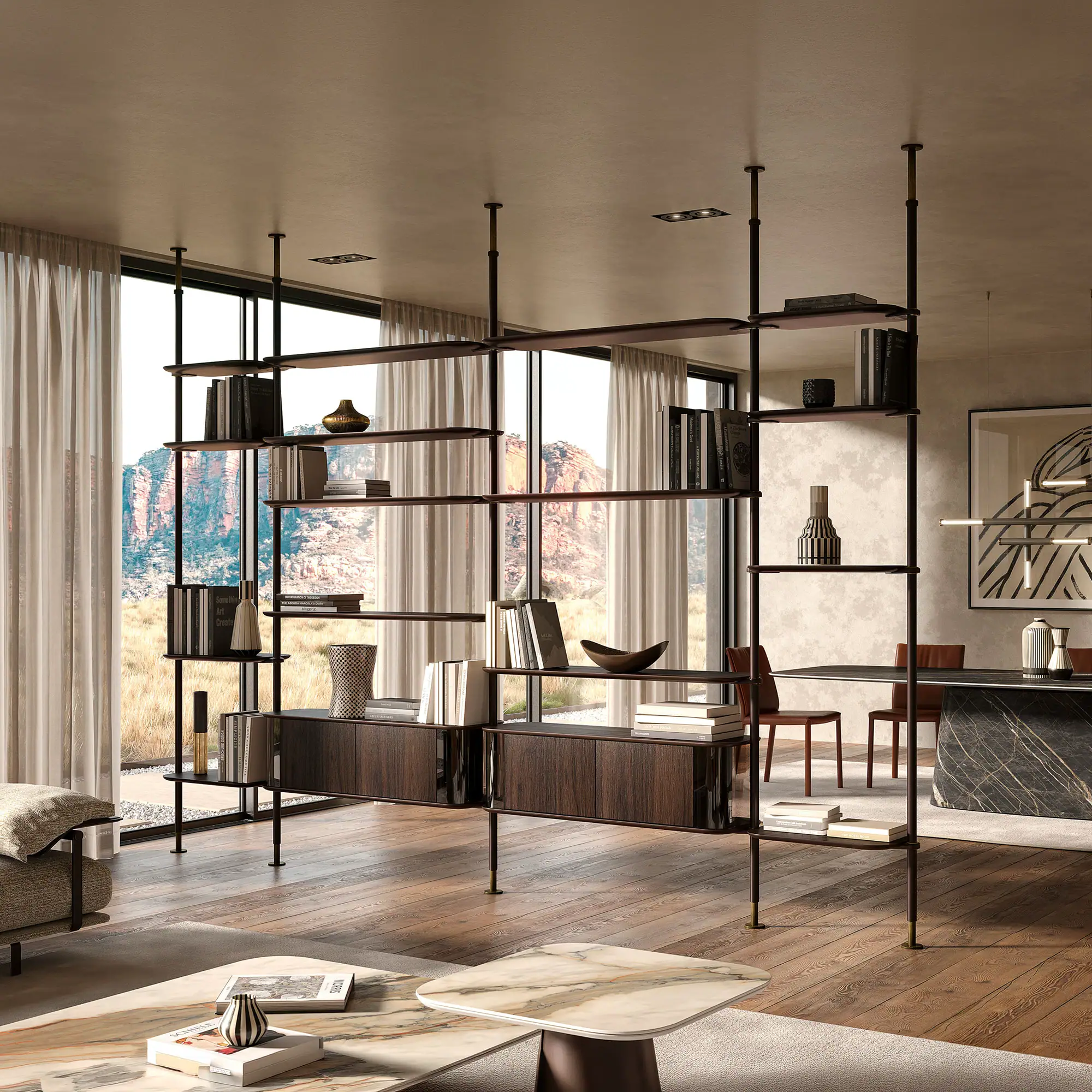 A modern living room with a dark wood and metal shelving unit acting as a room divider, filled with books and decor. Large windows overlook rocky mountains and dry grass. A dining area is visible to the right, and a marble coffee table is in the foreground.