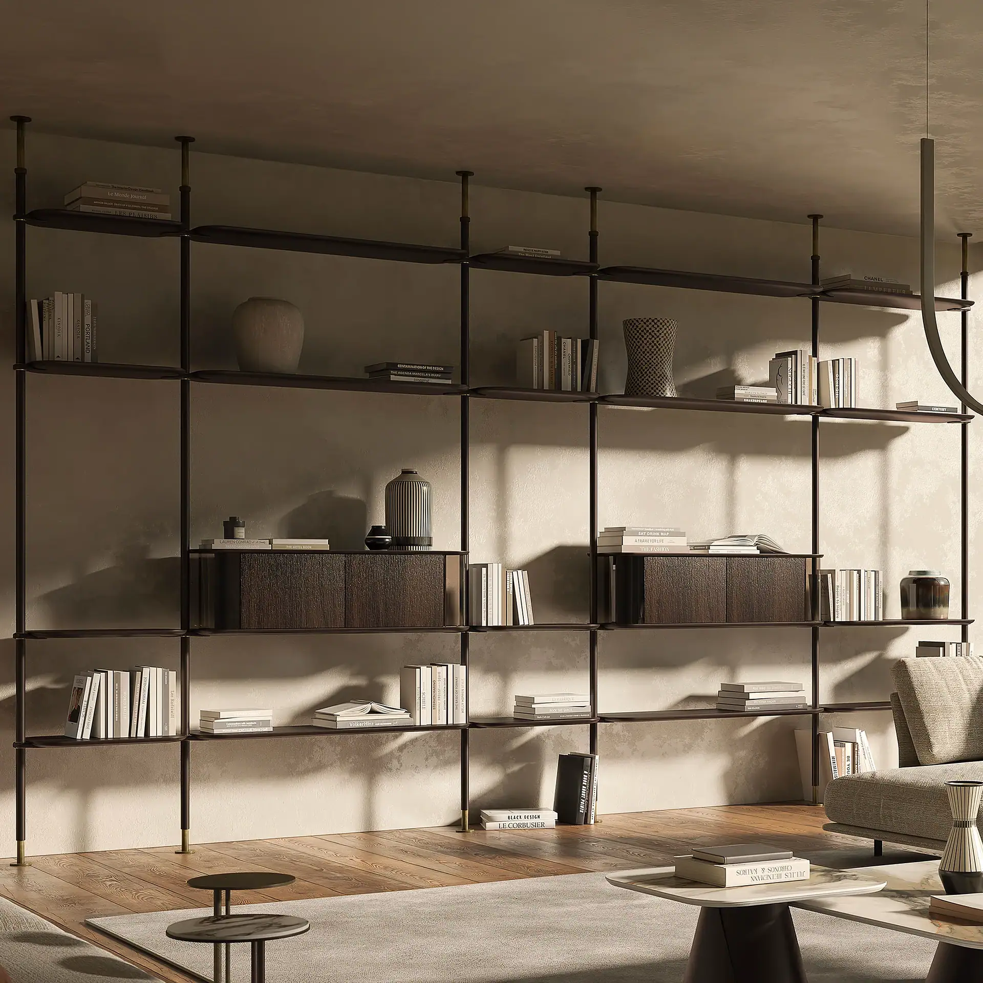 A modern living room with a large, dark modular shelving unit filled with books and decorative vases. A light gray rug covers a wooden floor, with coffee tables and a sofa in the foreground.